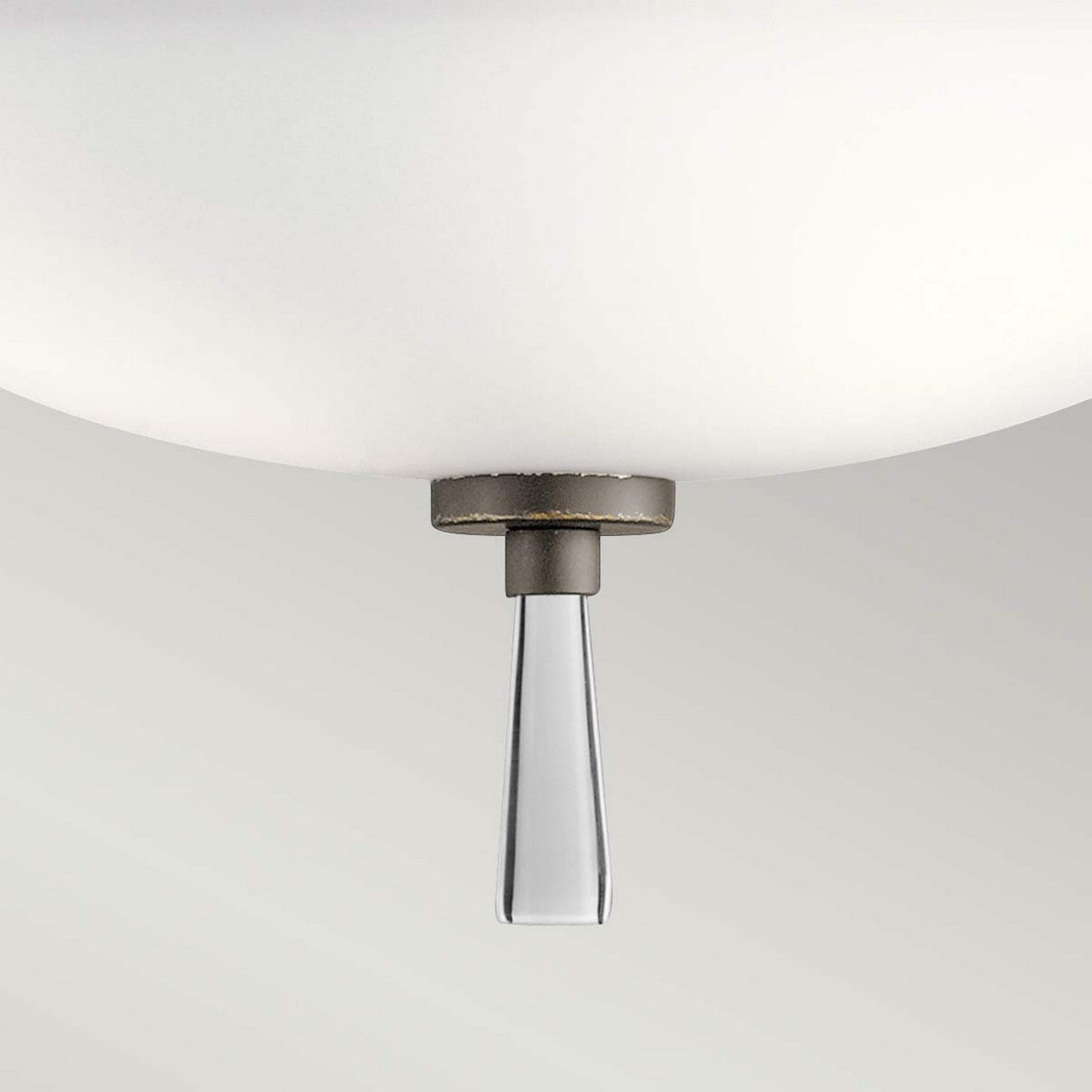 The Dreyfus 3 Light Semi Flush in Olde Bronze features a close-up of its white spherical lampshade, complemented by a sleek, tapered metal element and an optical crystal accent hanging below. The soft, neutral gradient background enhances the minimalist design of this light fixture.