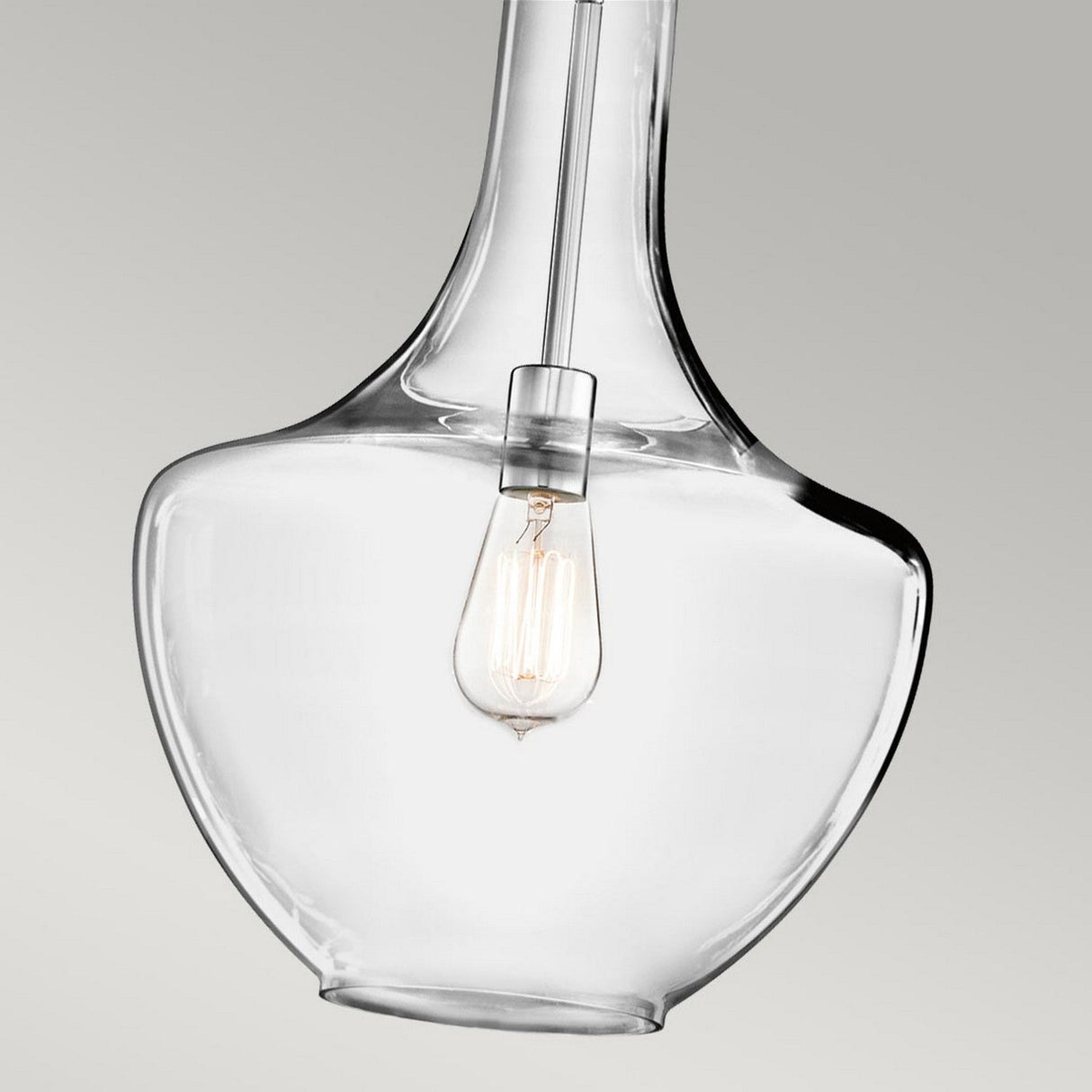 The Everly 1 Light Medium Pendant in Chrome, featuring a clear glass shade and vintage-style LED filament bulb, is set against a plain grey background to highlight its modern and minimalist design.