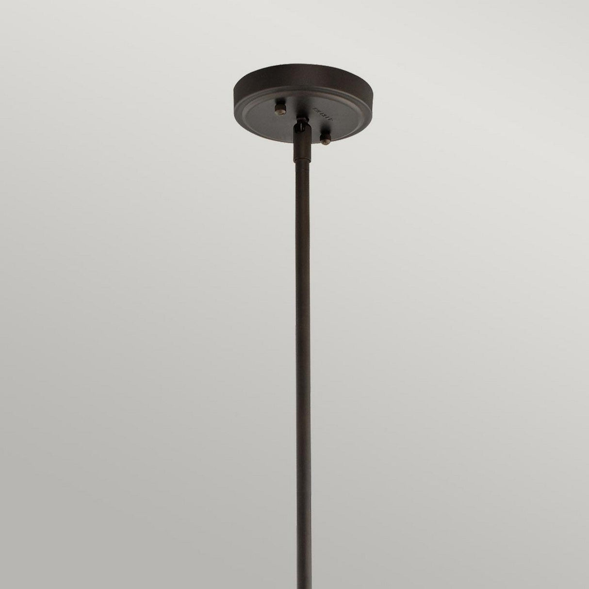 A minimalist black ceiling-mounted rod extends downward from a round base against a plain light gray background, evoking the sleek lines of the Everly 1 Light Medium Pendant. Its subtle elegance could be perfectly highlighted by an Olde Bronze finish for added sophistication.
