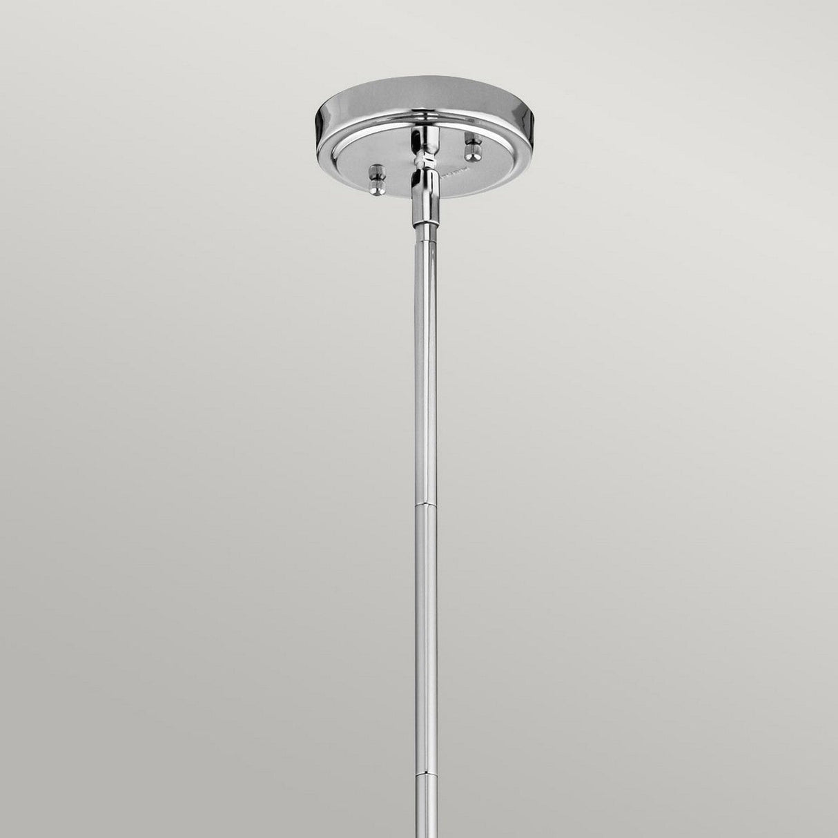 The Everly 1 Light Small Pendant - Chrome features a sleek chrome ceiling mount, where a rod elegantly extends downward to embody a sophisticated pendant lighting design. Its glossy round base shimmers against the plain gray background, highlighting the elegance of its chrome finish without any additional fixtures attached.