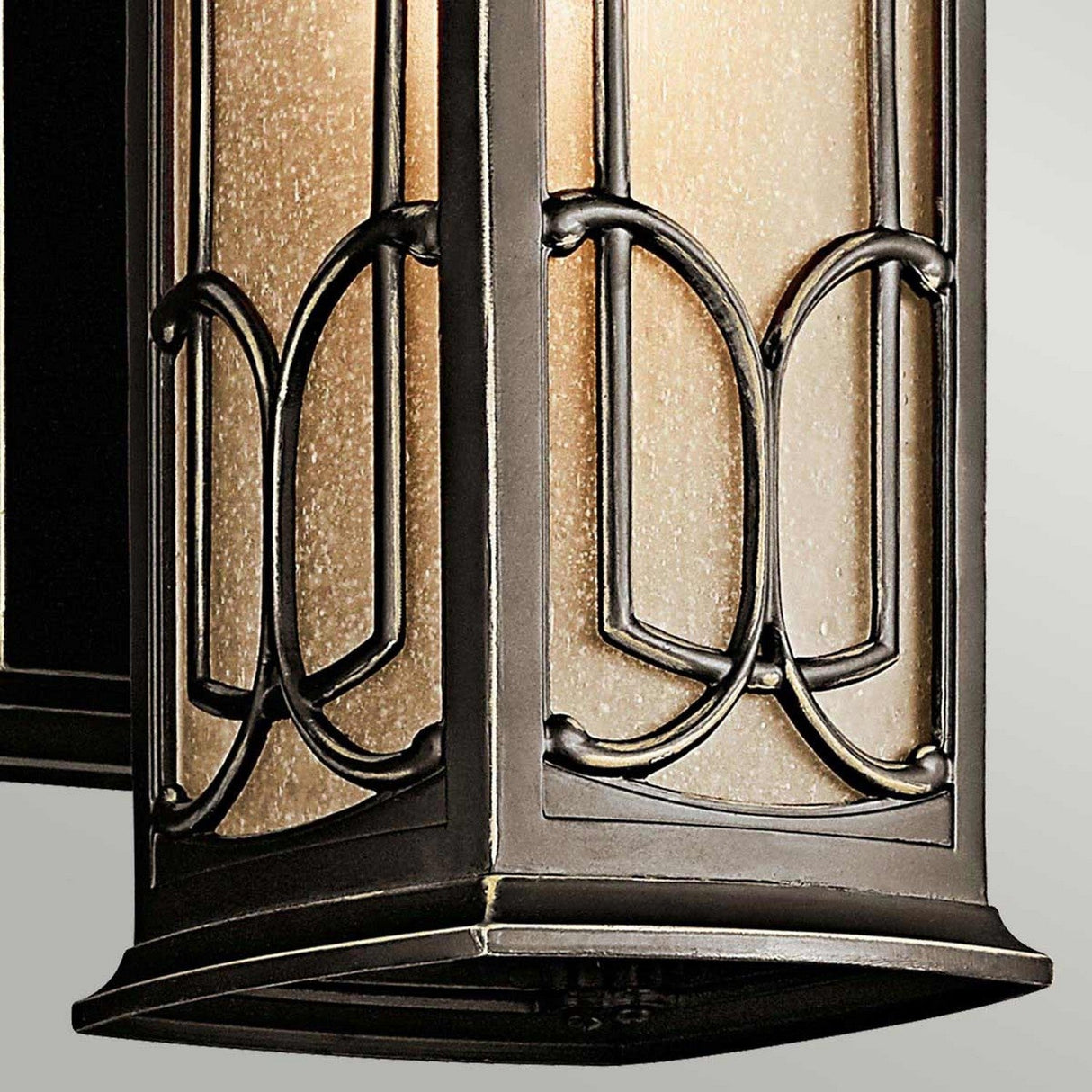 A close-up of the Franceasi Outdoor 1 Light Small Wall Lantern showcases its decorative design, featuring a metal frame with amber-tinted glass. The lantern's intricate, symmetrical design and Olde Bronze finish evoke a vintage or classic style.