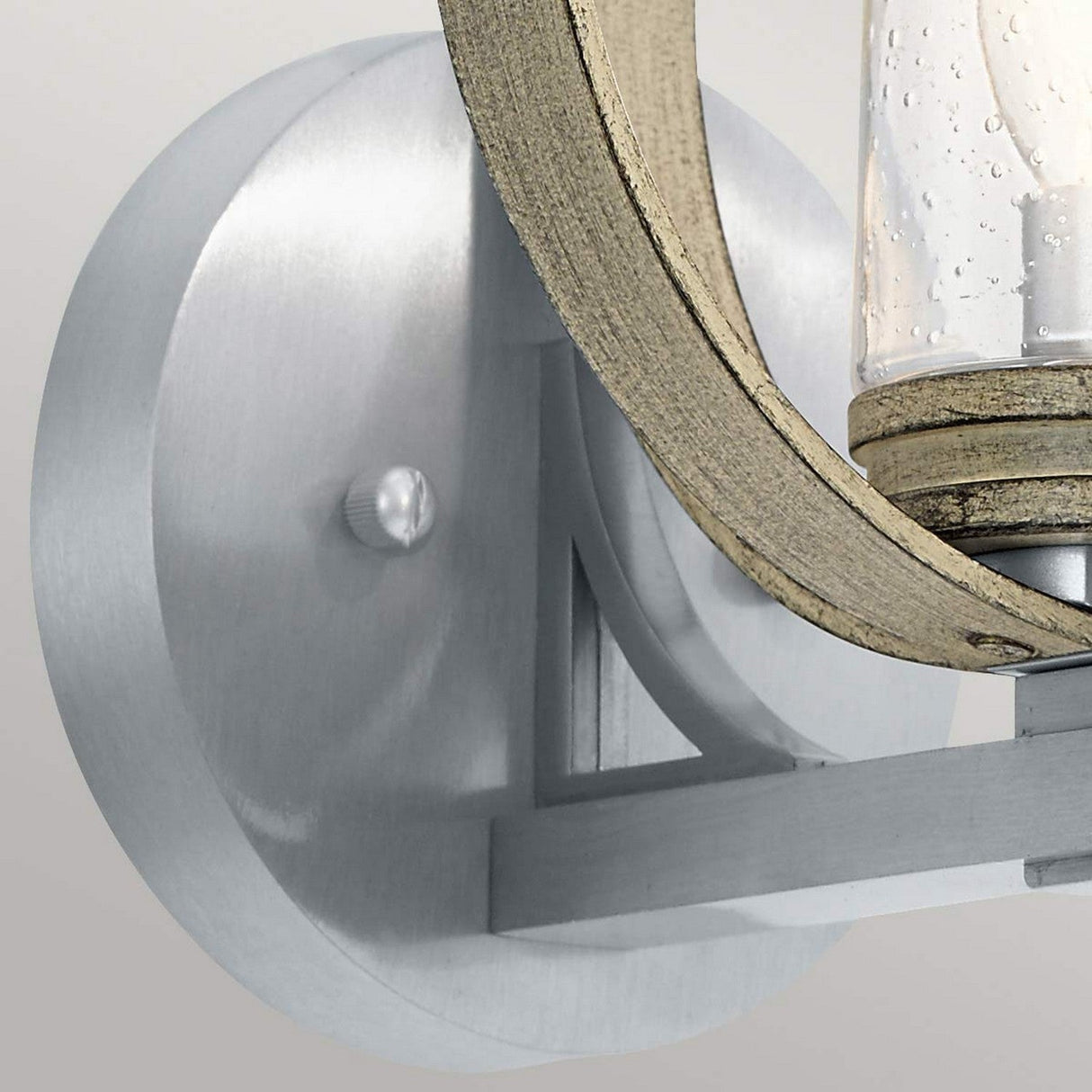 A close-up of the Grand Bank Outdoor 1 Light Wall Light shows its silver metal sconce with a circular base and a wooden hoop design. The glass enclosure, featuring a bubbled texture, adds charm while its IP44 rating ensures durability. The antique grey finish harmoniously complements the brushed aluminium against the plain gray background.