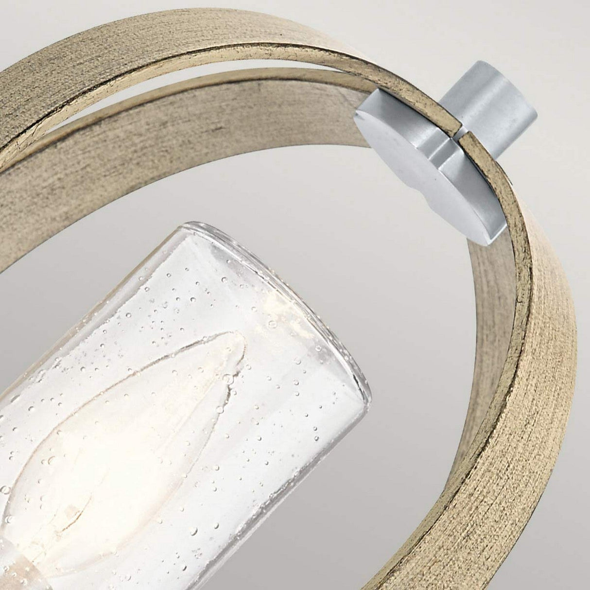 Close-up of the Grand Bank Outdoor 1 Light Wall Light, an IP44-rated light bulb encased in a glass cover with a wooden frame. This rustic fixture, held by a metallic connector, showcases an antique grey finish alongside brushed aluminium accents. Set against a plain, light background, this stylish piece is perfect for outdoor use as a wall light.