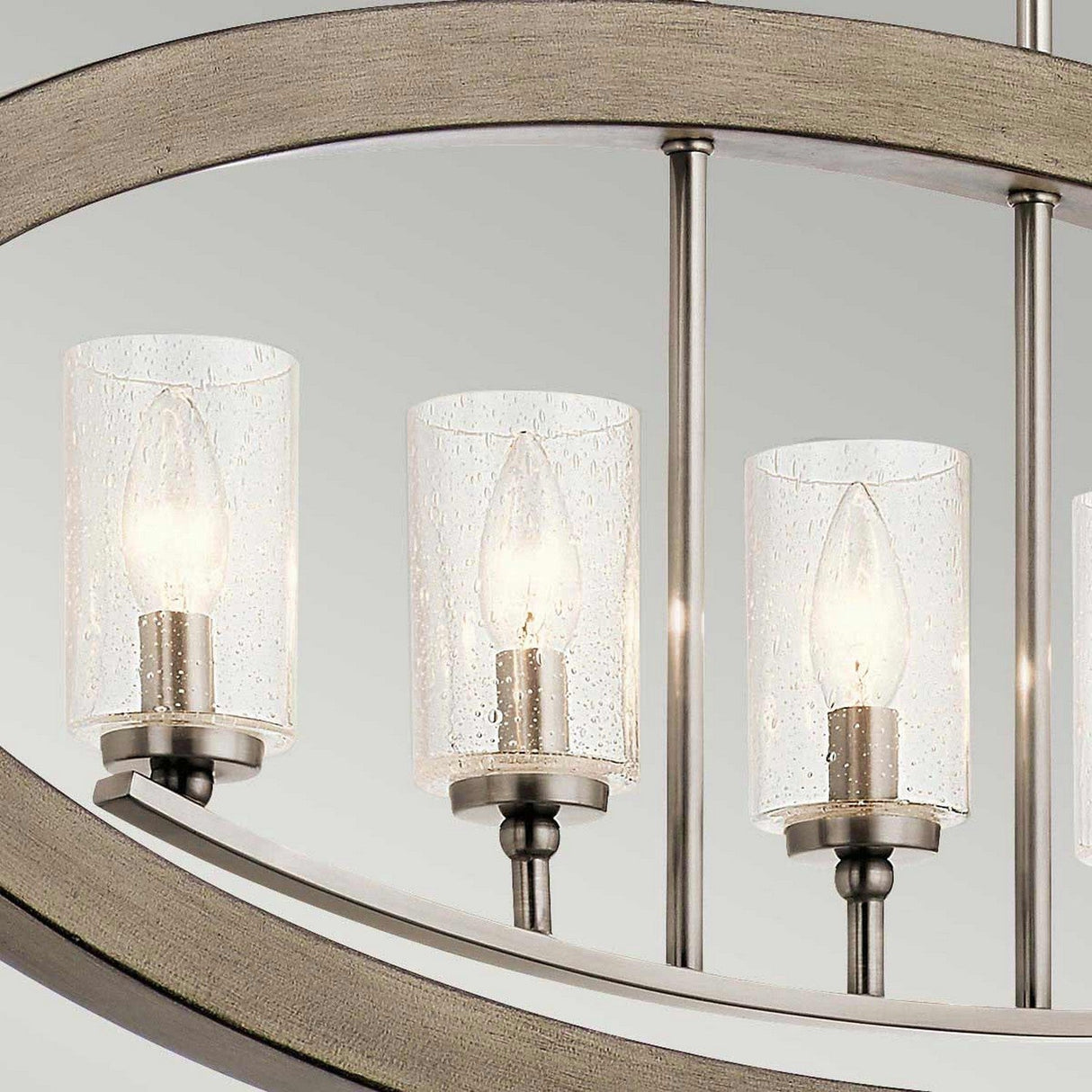 Close-up of the Grand Bank 5 Light Chandelier in Antique Grey, featuring cylindrical glass covers with a speckled texture that encase candle-shaped light bulbs. This fixture elegantly combines metal and wood, showcasing a contemporary design.