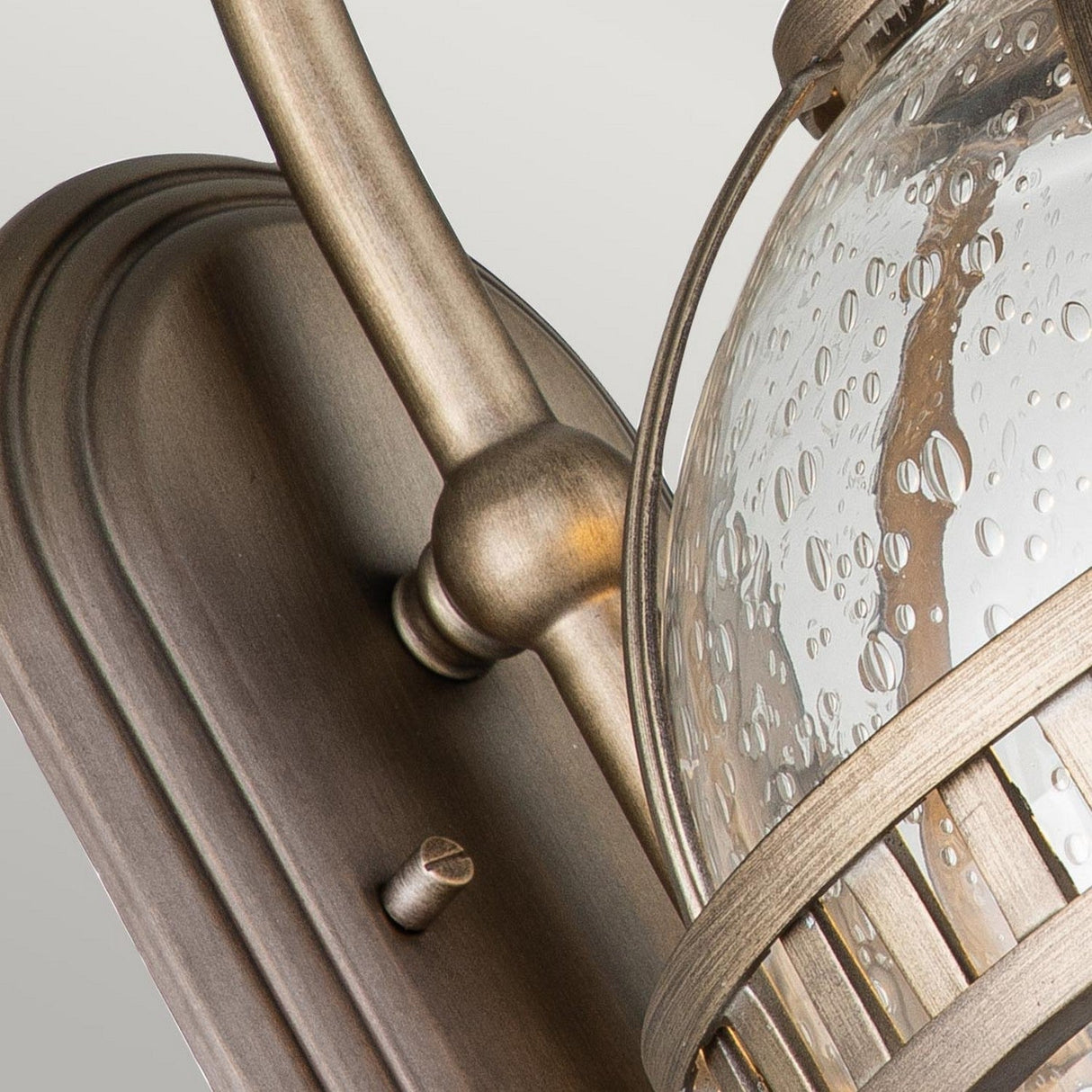 The Halleron Outdoor 2 Light Wall Lantern features a Victorian-style design, highlighted by its burnished bronze finish and clear glass shade with textured raindrop patterns. This elegant fixture includes a gracefully curved arm, adding to its vintage appeal.