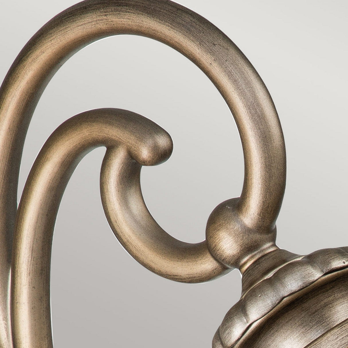 Close-up of an elegant detail on the Halleron Outdoor 2 Light Wall Lantern in burnished bronze against a light gray background. The flowing design and polished finish evoke the charm of Victorian-era lighting.