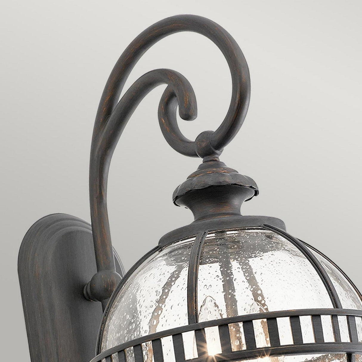 A close-up of the Halleron Outdoor 2 Light Wall Lantern highlights its grey metal finish with clear seeded glass. Its curved arm and dome design evoke Victorian-inspired charm, adding an elegant touch ideal for traditional exterior lighting.