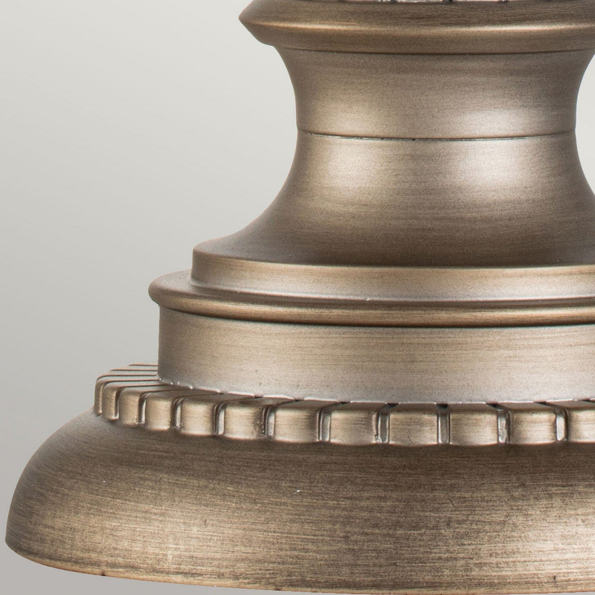 A close-up of a burnished bronze metal fixture with a textured, ridged design evocative of Victorian Era lighting, featuring a rounded base with decorative detailing and a smooth finish, similar to the Halleron Outdoor 3 Light Pedestal Pendant.