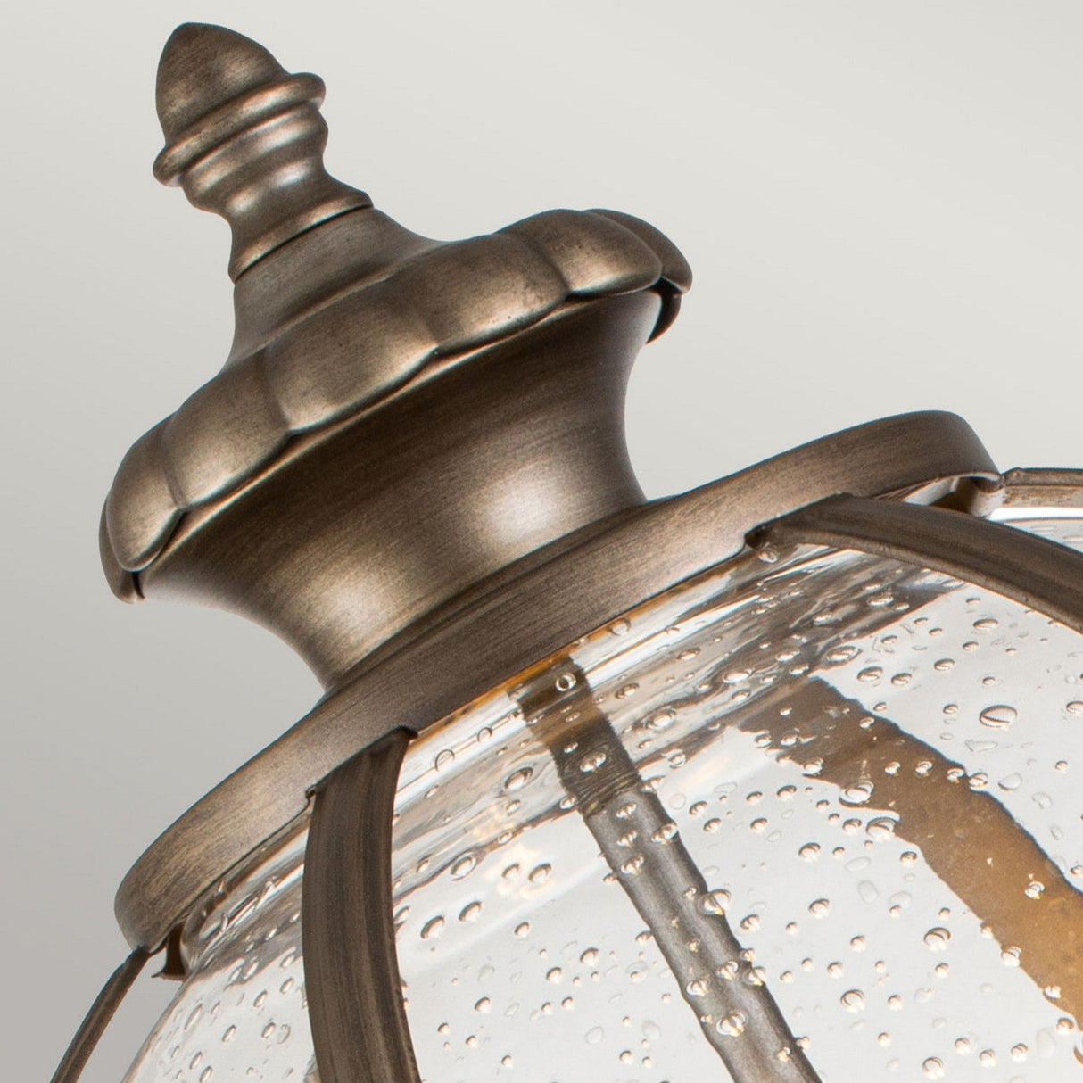 Close-up of a Victorian era Halleron Outdoor 3 Light Pedestal Pendant. The lamp features a burnished bronze finish with a decorative top and clear, bubbled glass panels.