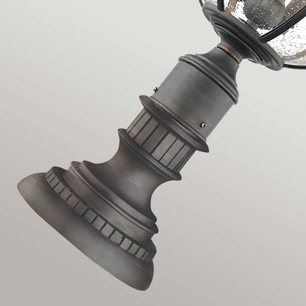 Close-up of the Halleron Outdoor 3 Light Pedestal Lantern, showcasing a dark grey matte finish with decorative grooved accents. Reminiscent of a Victorian-inspired lantern, the lamp is slightly tilted against a neutral background.