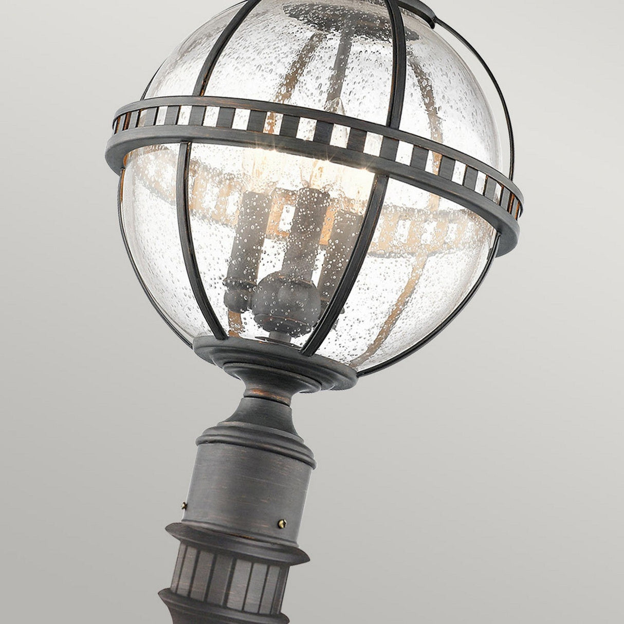 Inspired by the Victorian era, the Halleron Outdoor 3 Light Pedestal Lantern in Grey features a vintage-style design with a spherical glass bulb encased in a weathered metal frame. The bulb emits a soft light, visible through the textured glass surface. This IP44 rated fixture boasts a classic elegant design that is perfect for any outdoor setting.