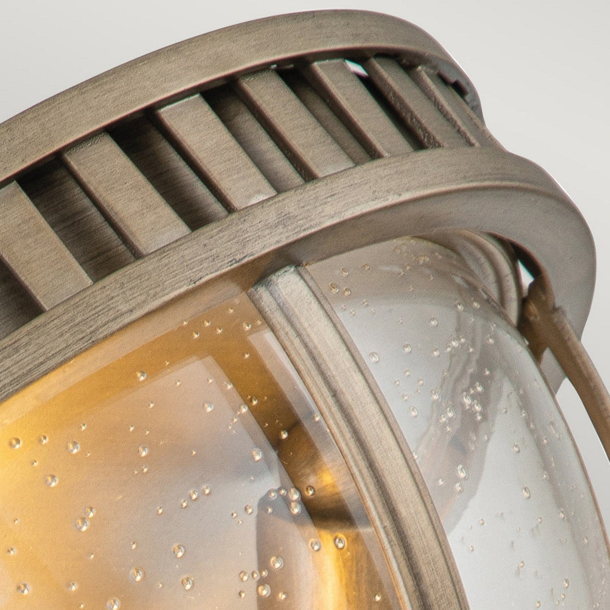 Close-up of the Halleron Outdoor 3 Light Ceiling Flush in burnished bronze, featuring a clear, bubble-textured glass cover. The grid-like metal design at the top enhances its Victorian-style aesthetic, adding vintage charm to any space.