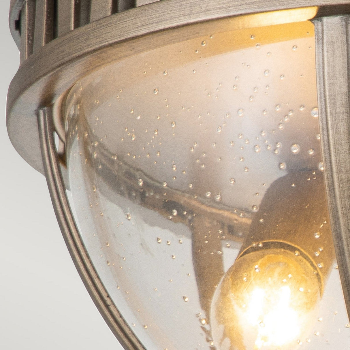 Close-up of the Halleron Outdoor 3 Light Ceiling Flush in burnished bronze, featuring a frosted glass cover speckled with condensation. This Victorian-style light fixture has a metallic frame and encloses a luminous bulb within.
