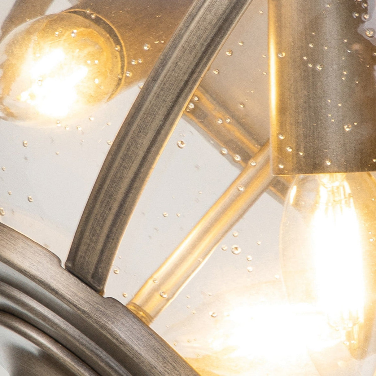 Close-up of the Halleron Outdoor 3 Light Ceiling Flush, showcasing its burnished bronze metal frame and glass cover. The textured glass, embellished with small bubbles, enhances its Victorian-style design. Inside, the bulbs are illuminated, emitting a warm glow.