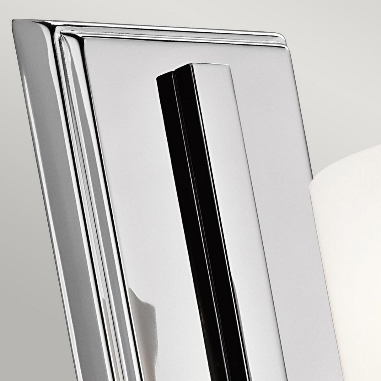 A close-up of the Hendrik 1 Light Wall Light in polished chrome showcases its modern, sleek metal design. Its clean geometric lines and reflective surface exude contemporary elegance, making it ideal for sophisticated bathroom lighting against a neutral backdrop.