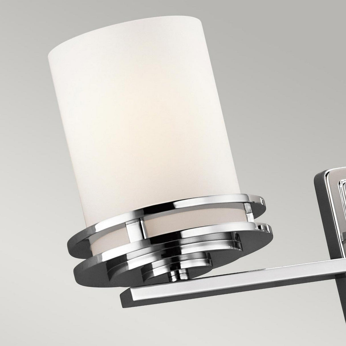 A close-up of the Hendrik 3 Light Wall Light in polished chrome showcases its sleek modern design, featuring a cylindrical white lampshade set against a gray background. With its IP44 rating, it is perfect for bathroom lighting.