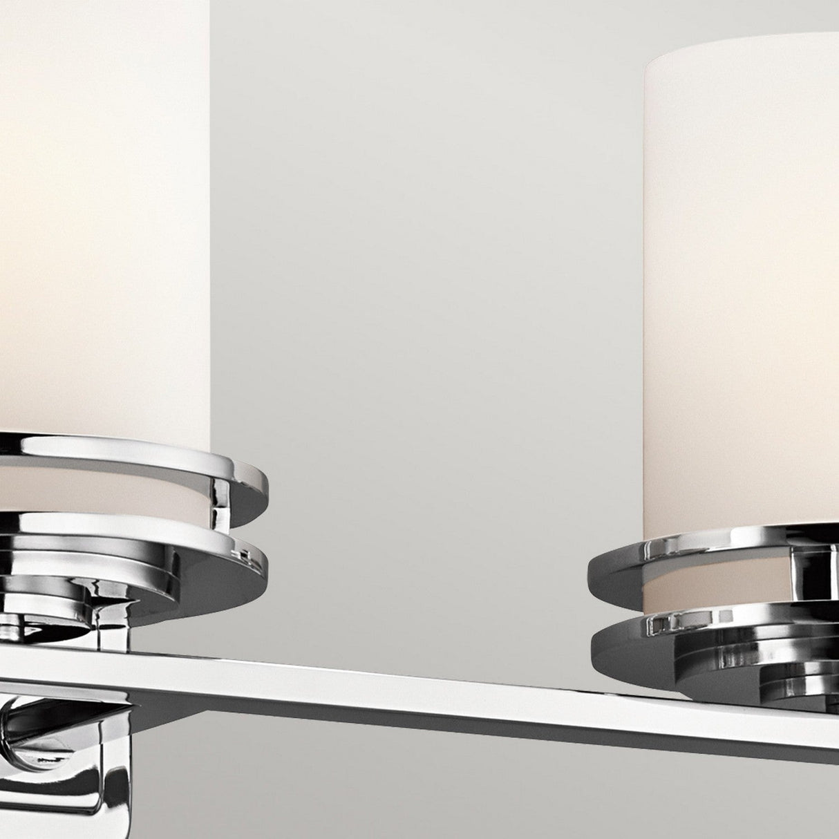 Close-up of the Hendrik 3 Light Wall Light in polished chrome, showcasing two cylindrical white frosted glass shades. This modern fixture is ideal for bathroom lighting with its IP44 rating and is beautifully mounted on a horizontal bar with a minimalist design against a plain gray background.