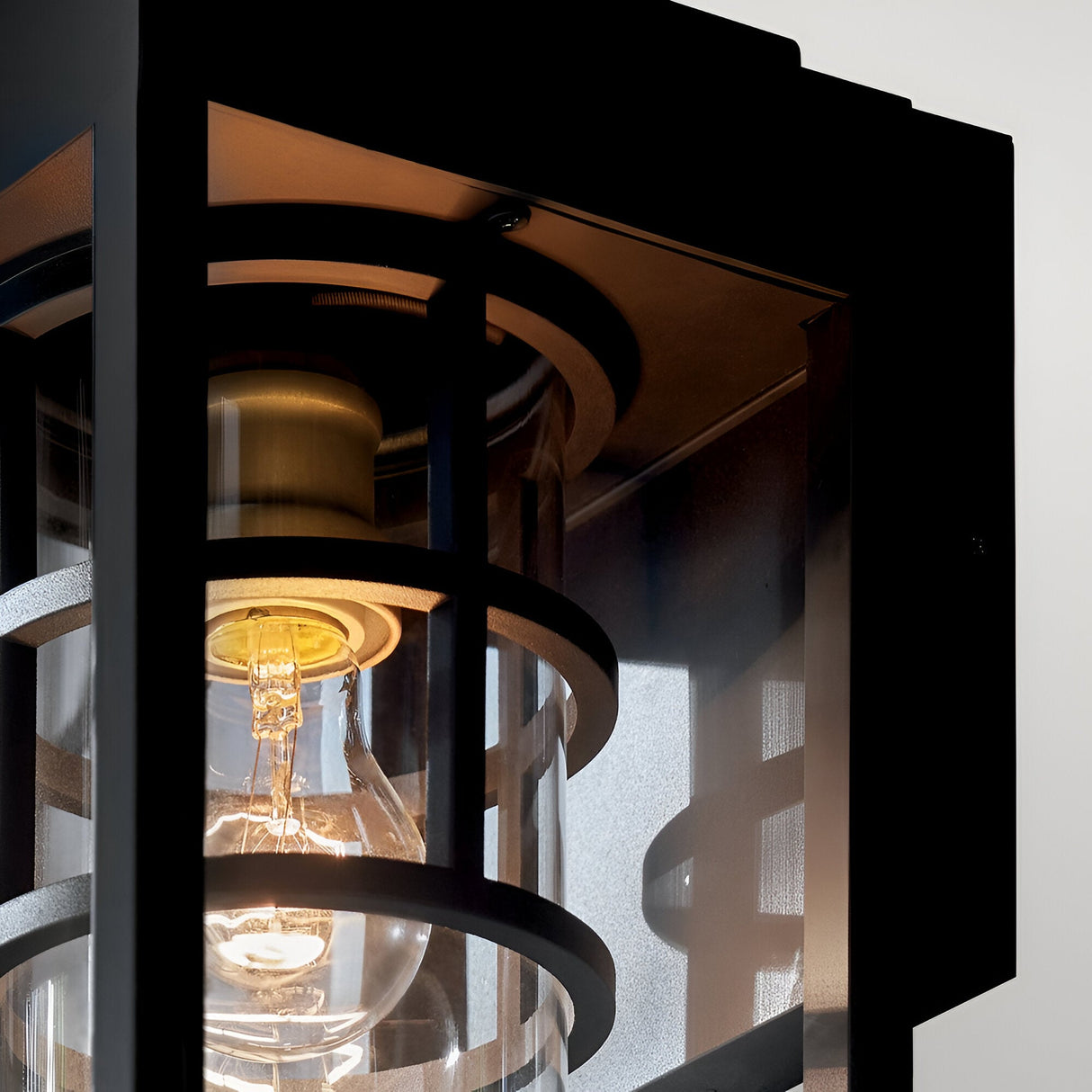 Close-up of the Hone Coastal 1 Light Medium Outdoor Wall Lantern in black, featuring a visible bulb, black metal housing, and glass panels. Its geometric design is both industrial and weather-resistant—ideal for outdoor use.