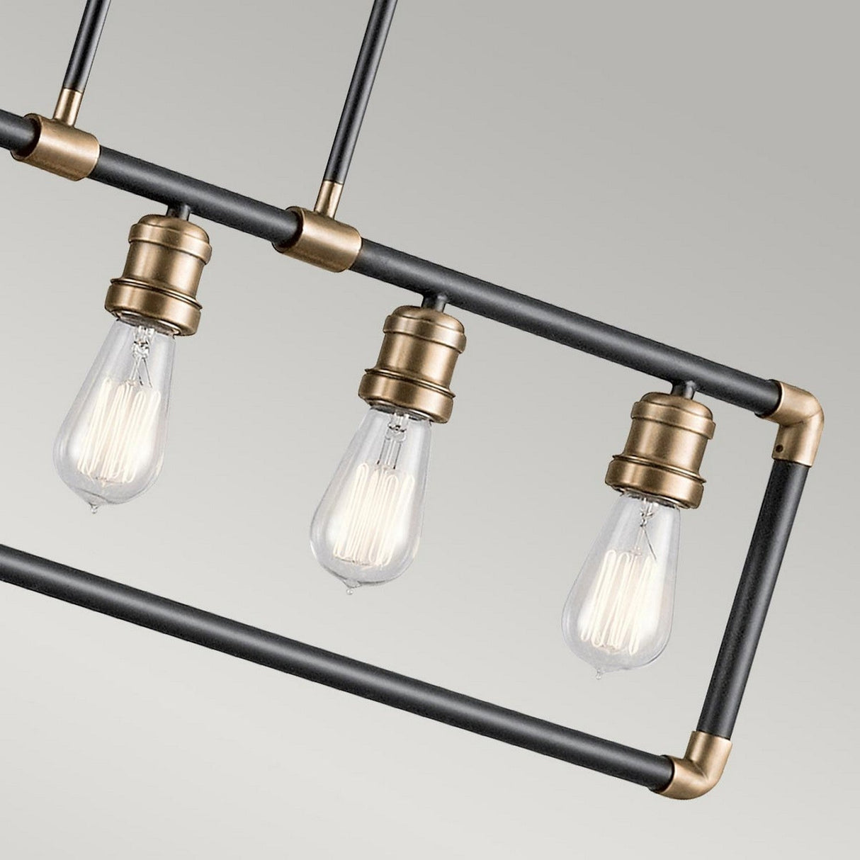 The Imahn 5 Light Bar Pendant showcases a modern industrial design with three exposed Edison-style LED bulbs suspended from a rectangular metal frame. The matte black finish, accented with natural brass, adds an elegant touch to any contemporary bar pendant setup against a light gray backdrop.