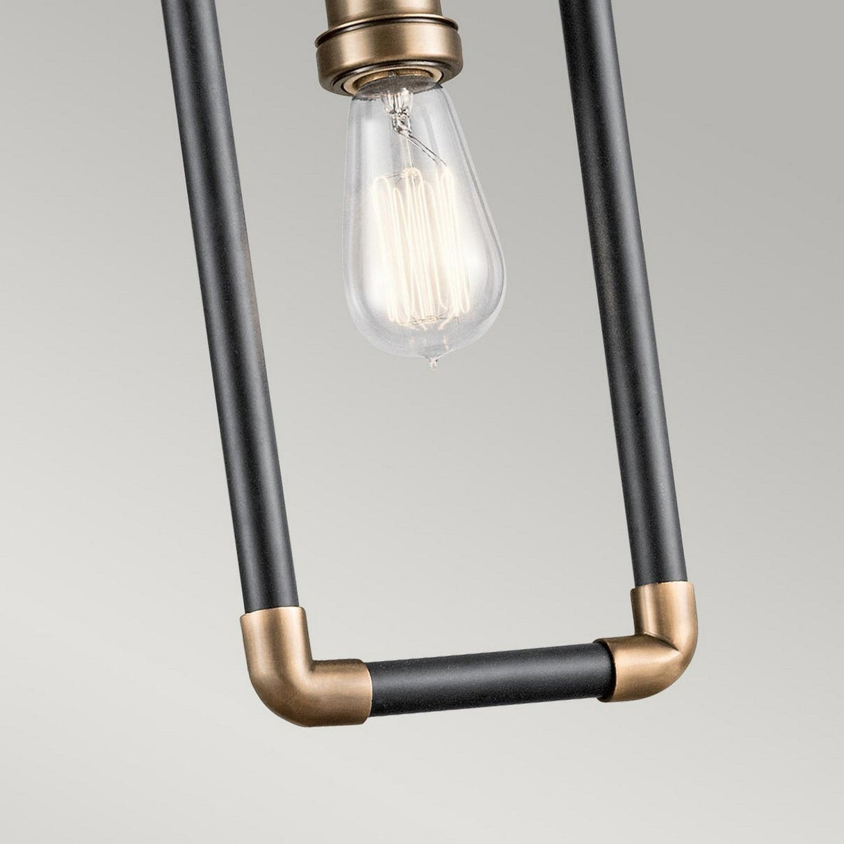 The Imahn 1 Light Mini Pendant adds an industrial touch with its exposed Edison-style LED filament bulb. The fixture features a rectangular black metal frame highlighted by natural brass accents, beautifully framing the bulb as it emits a warm glow against a neutral backdrop.