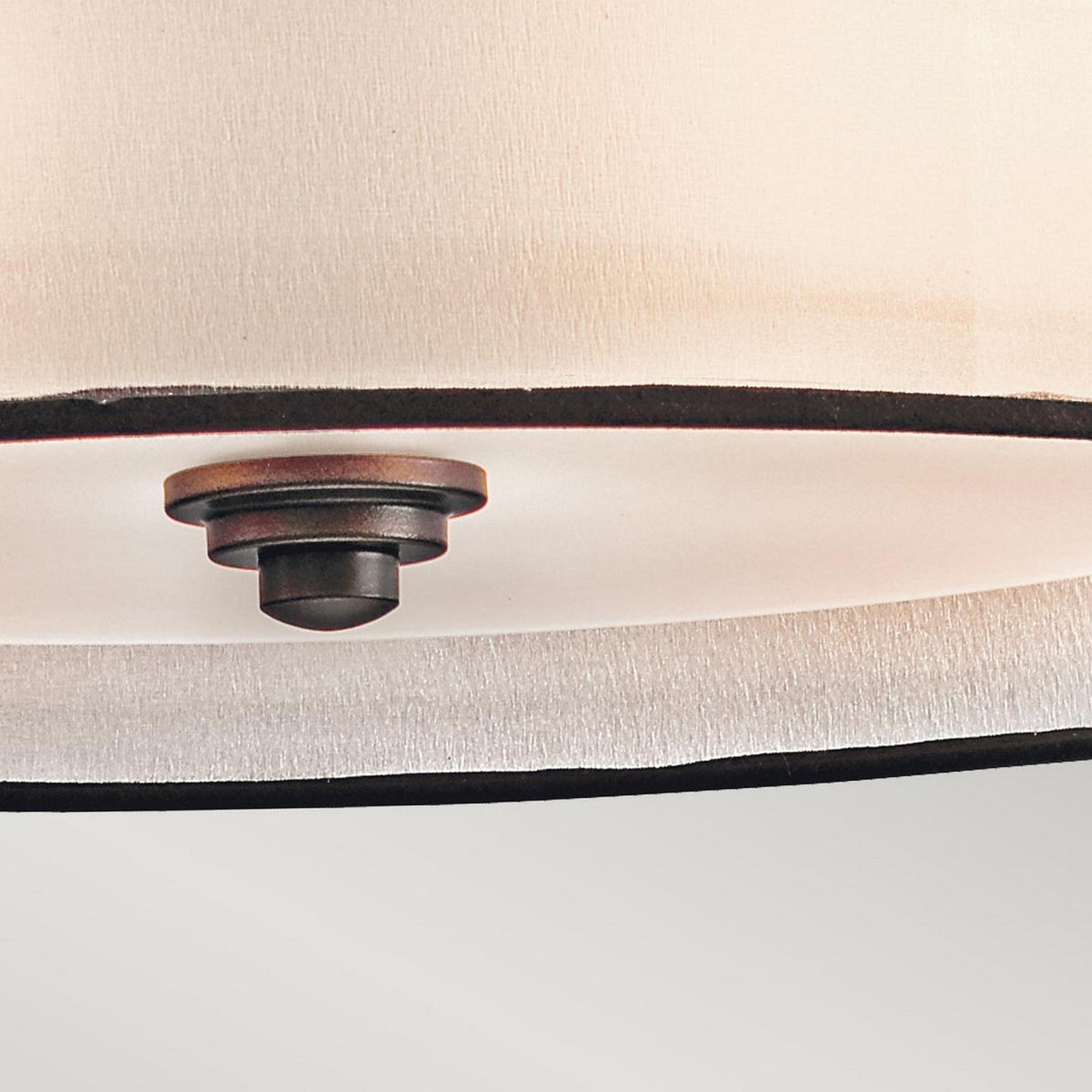 Close-up of the Lacey 4 Light Large Pendant in Bronze, showcasing its elegant round beige fabric shade with black trim. A central black knob secures the shade, exuding sophisticated charm against a plain light gray wall with its understated design.