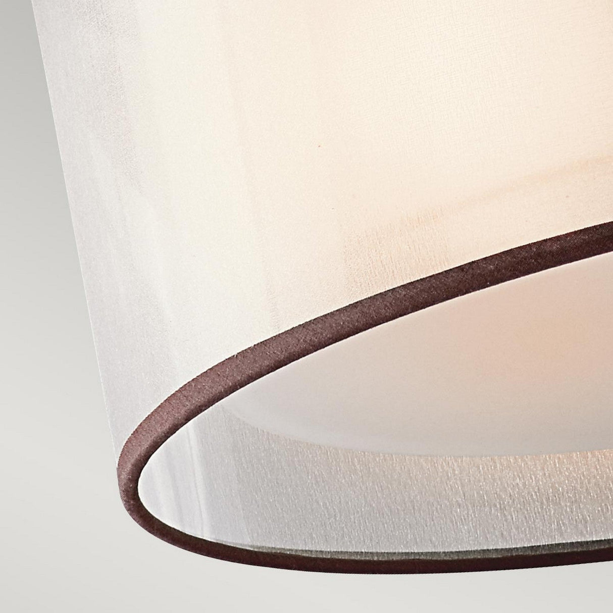 Close-up of the beige lampshade with brown trim from the sophisticated Lacey 3 Light Small Semi Flush - Bronze. The fabric texture highlights its soft curves and subtle lighting against a plain light gray background.