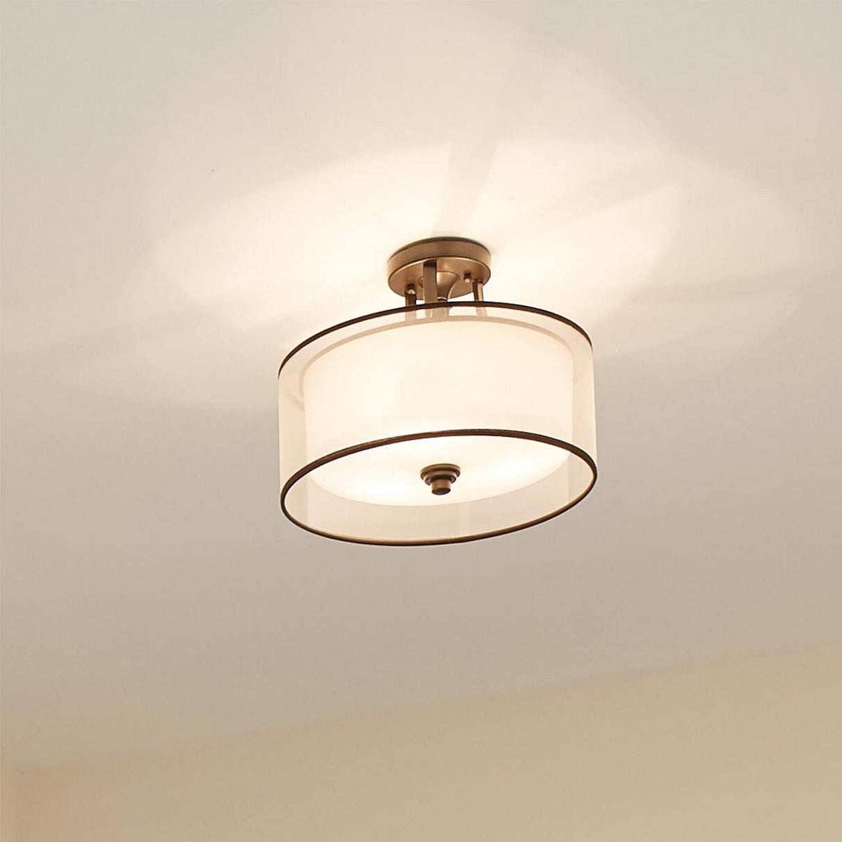 The Lacey 3 Light Small Semi Flush - Bronze showcases an elegant double-shade design with a simple white drum shape, casting a warm glow on the ceiling.