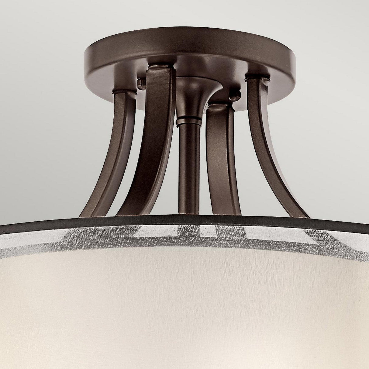 A close-up of the Lacey 4 Light Semi Flush - Bronze reveals a metal frame with a bronze finish and a beige fabric lampshade. This modern lighting fixture boasts a sophisticated double-shade design, ideal for complementing any contemporary setting.