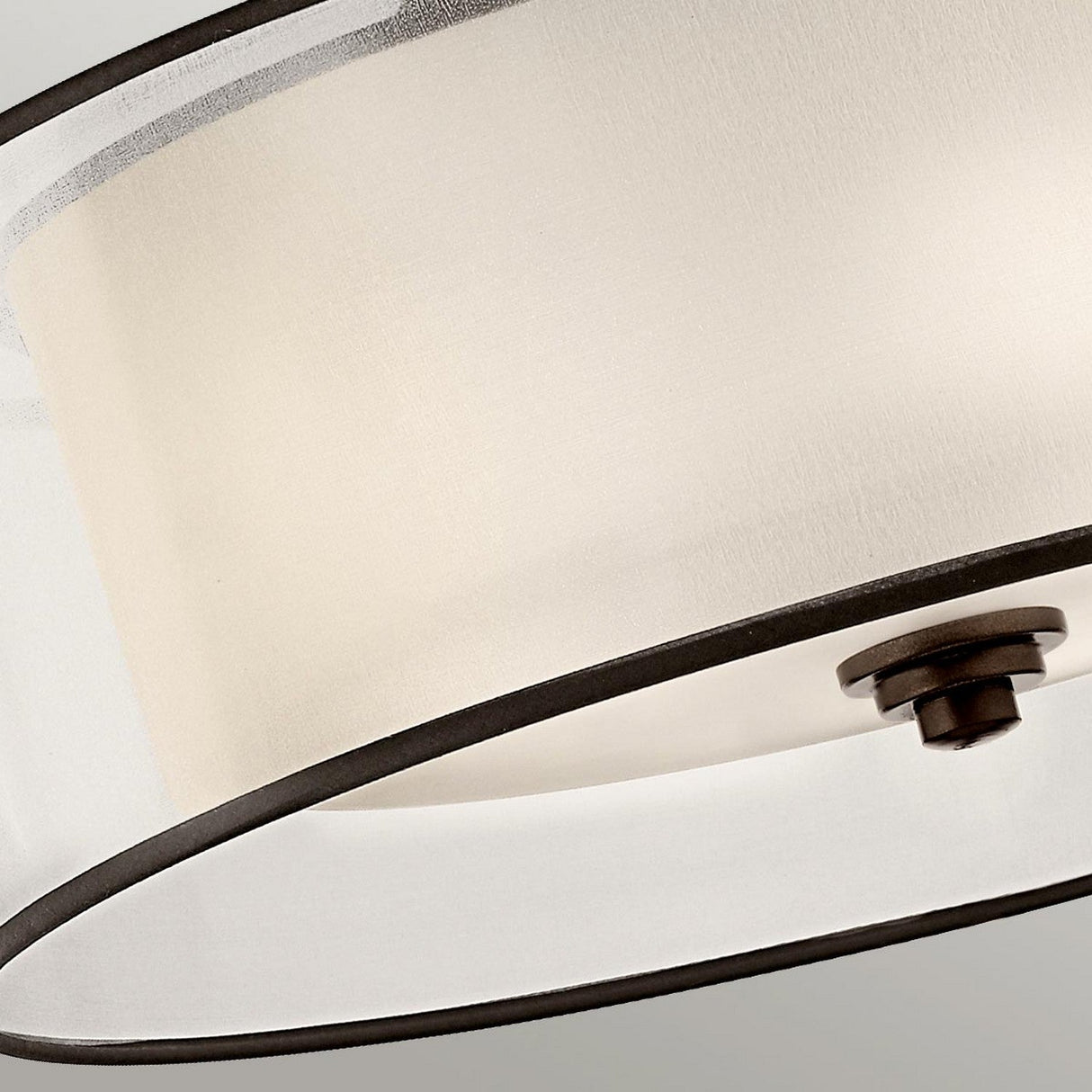 Close-up of a contemporary ceiling lamp with a cylindrical white fabric shade and dark bronze trim, showcasing a circular metal detail in the center. This elegant fixture, described as the Lacey 4 Light Semi Flush - Bronze, is set against a light gray background.