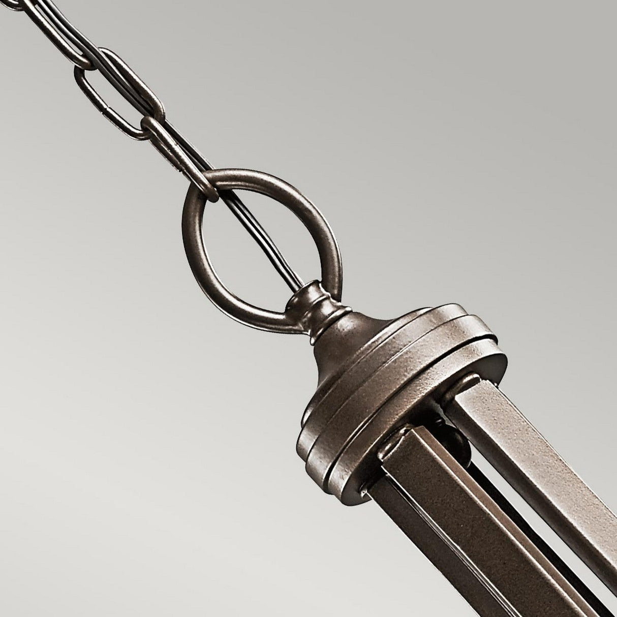 Close-up of the Lacey 5 Light Chandelier - Bronze, hanging from a chain against a neutral background. The chandelier features a bronze finish with geometric design elements, reminiscent of transitional interiors, attached to a cable with a circular ring.