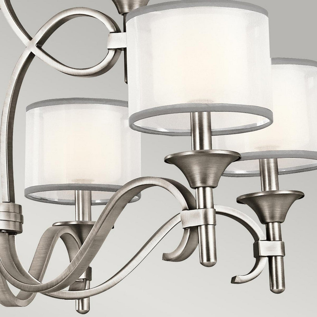 Close-up of the Lacey 9 Light Chandelier - Silver, featuring sleek brushed metal arms and three cylindrical white lampshades. The design boasts elegant curved lines with a modern finish set against a light gray background.