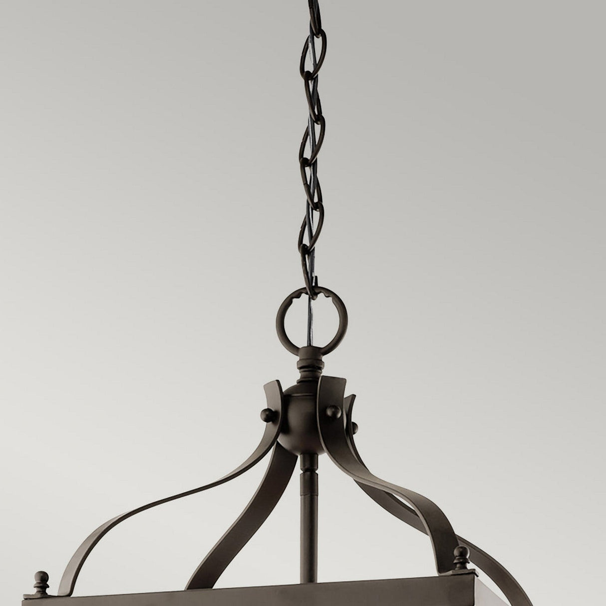 Close-up of the Larkin 3 Light Medium Chandelier - Olde Bronze in an open cage design, showcasing a twisted chain. The minimalist fixture's curved metal elements and ring top are highlighted against a plain gray background.