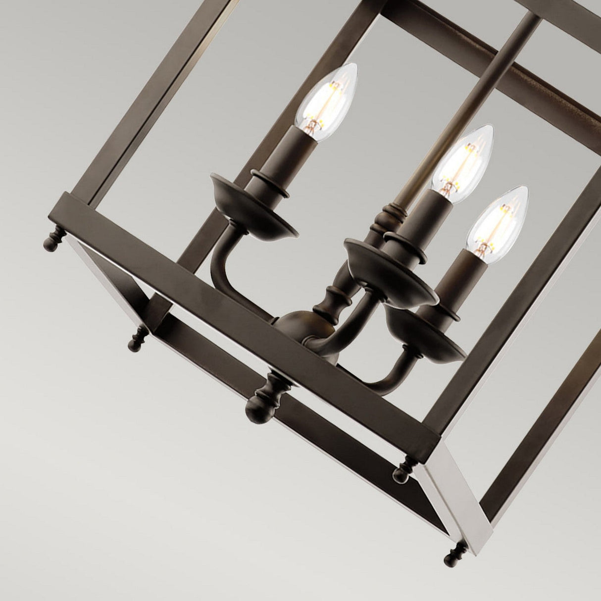 A close-up view of a Larkin Medium Chandelier in Olde Bronze, showcasing three candle-shaped light bulbs within an open cage design against a plain background.
