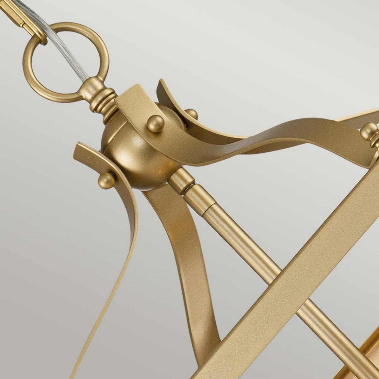 Close-up of a natural brass structure with curved and straight elements, showcasing an open cage design around a spherical pivot point and a decorative ring at the top. The intricate artistry resembles part of the Larkin 3 Light Medium Chandelier - Natural Brass.