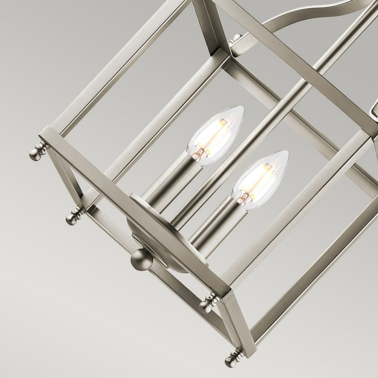 A close-up view of the Larkin 2 Light Small Chandelier in brushed nickel, showcasing its modern lantern-style with an open cage design and two exposed candle-shaped bulbs against a neutral background.