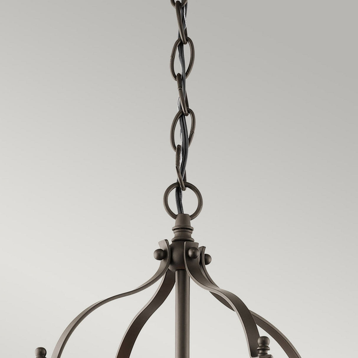 A close-up view showcases the intricate details of the decorative chain of the Larkin 2 Light Small Chandelier - Olde Bronze, set against a light gray background. The interlocking links of the chain lead to a captivating chandelier featuring an open cage design and gracefully curved metal elements, all elegantly finished in Olde Bronze.