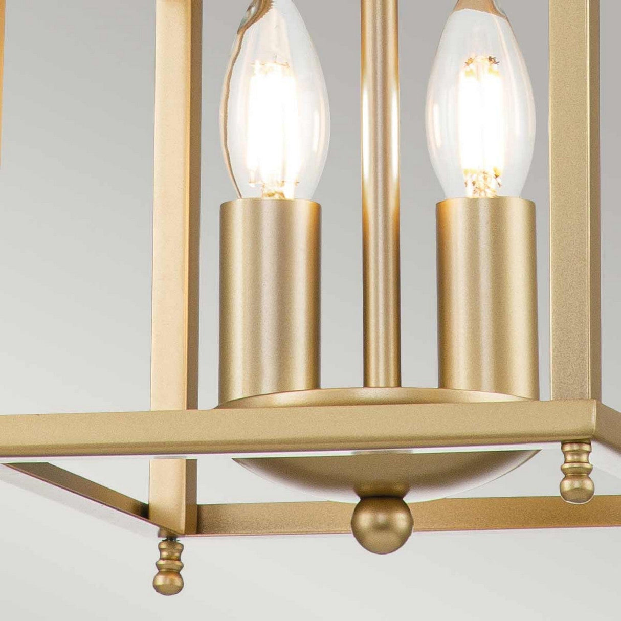 Close-up of the Larkin 2 Light Small Chandelier - Natural Brass, showcasing its minimalist open cage design and two glowing, candle-inspired light bulbs set within a natural brass frame defined by clean lines. The elegant design accentuates the warm glow of the bulbs against a neutral backdrop.