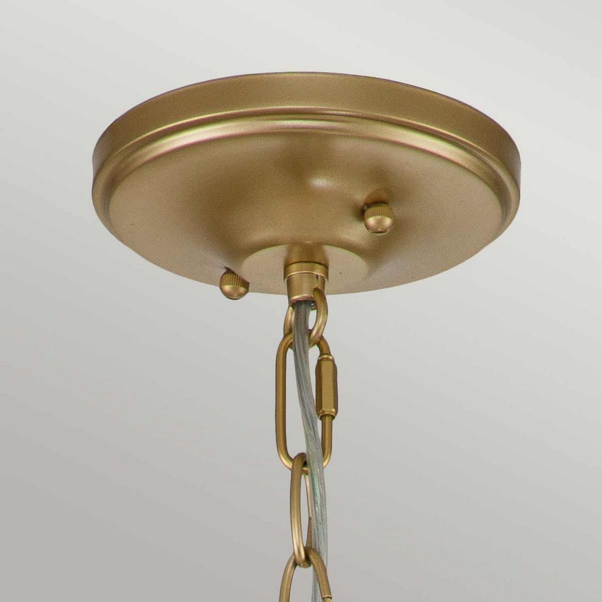 Close-up view of the natural brass ceiling canopy from the Larkin 2 Light Small Chandelier, featuring a hanging chain. The smooth, round surface is accentuated by two small decorative knobs, set against a soft gray background.