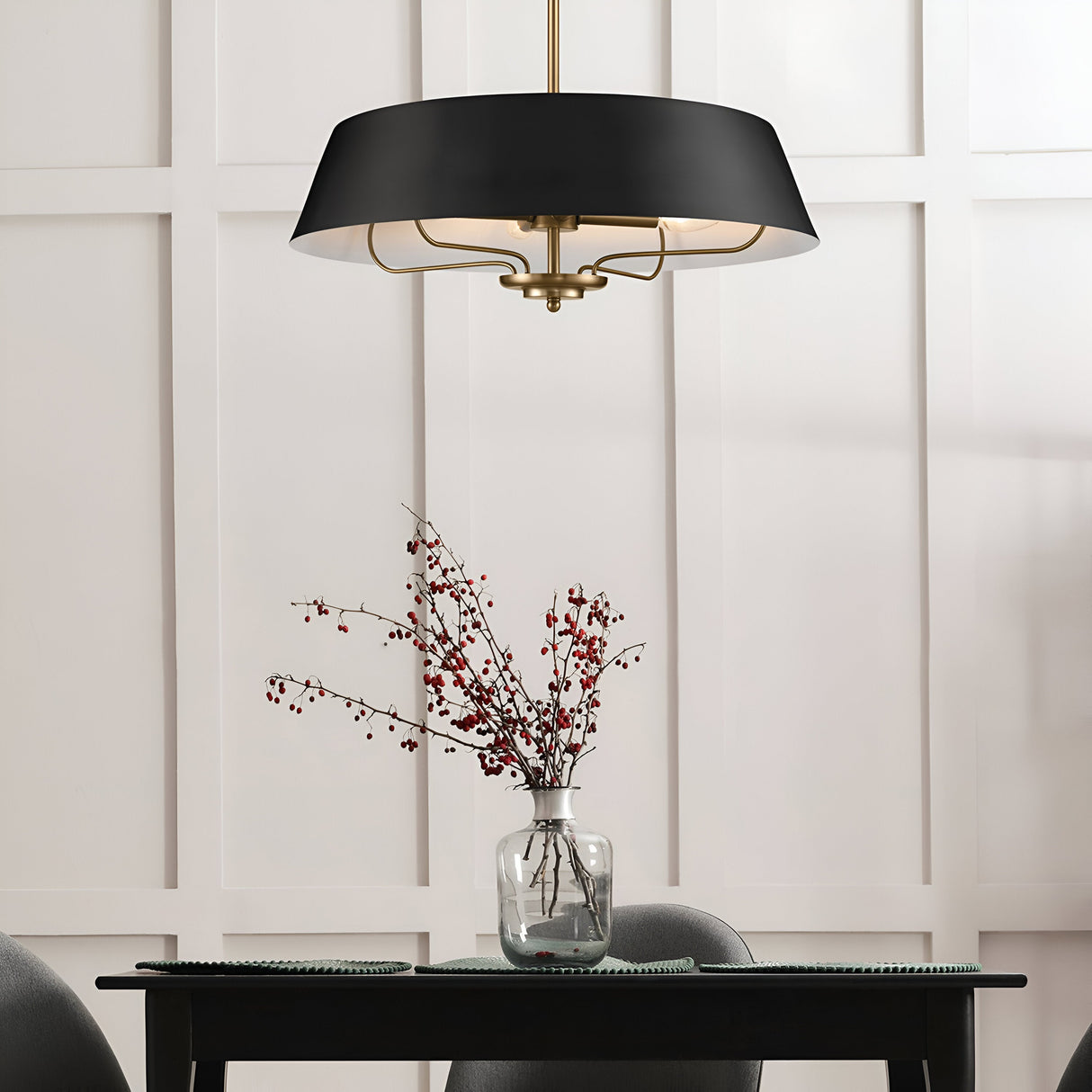 A contemporary dining space showcases the Luella 4 Light Duo-Mount Chandelier/Semi-Flush in Black & Brass beautifully positioned above a dark table, which is adorned with a clear vase containing branches of red berries. The chandelier's design harmonizes perfectly with the setting, against the backdrop of a white grid-patterned wall.