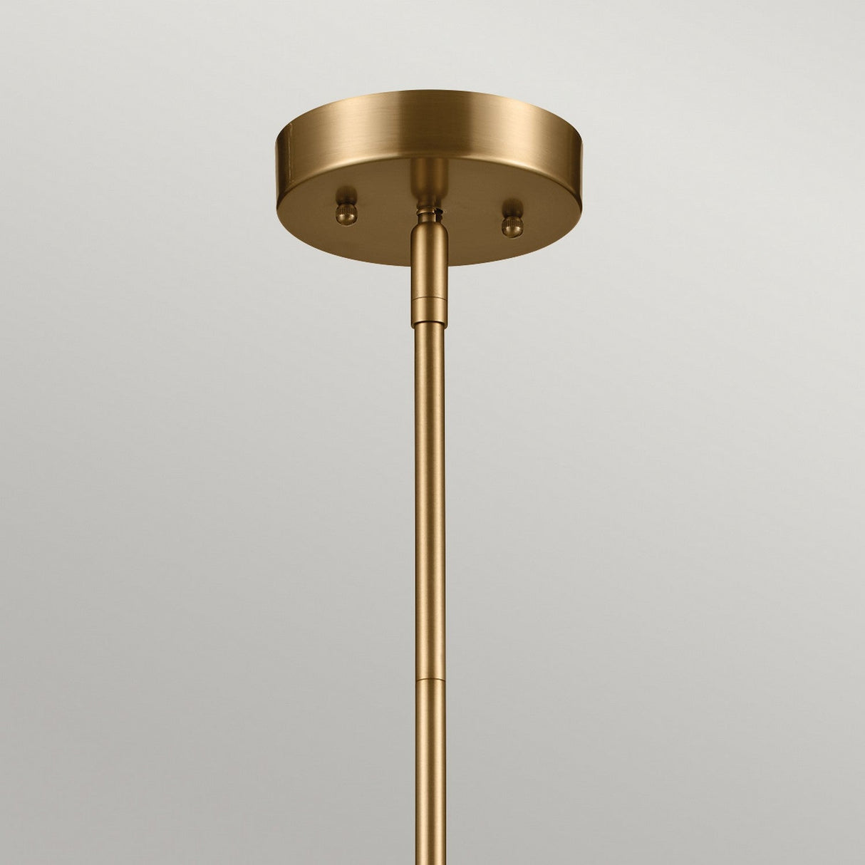 A detailed look at the Luella 4 Light Duo-Mount Chandelier/Semi-Flush in brushed natural brass, showcasing its cylindrical base and sleek, minimalist design. The fixture's smooth finish complements its elegant placement against a light gray ceiling.