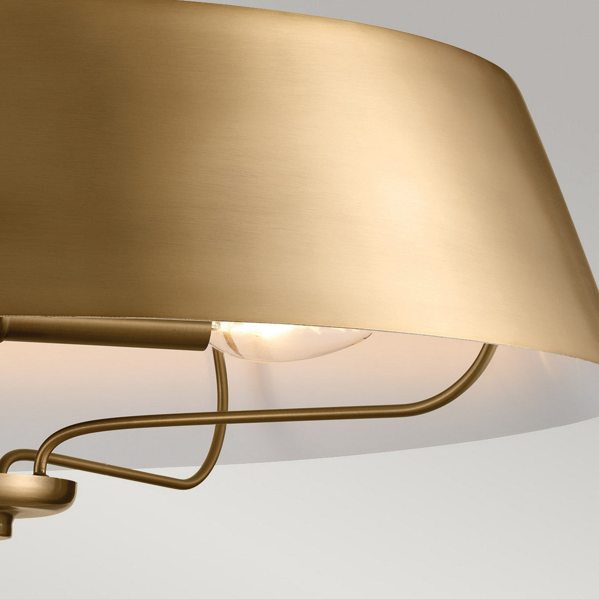 Close-up of the Luella 4 Light Duo-Mount Chandelier/Semi-Flush in brushed natural brass, featuring a sleek circular shade and visible light bulb against a soft gray background. The design showcases smooth, minimalist curves and a warm, reflective surface, offering versatile installation options.