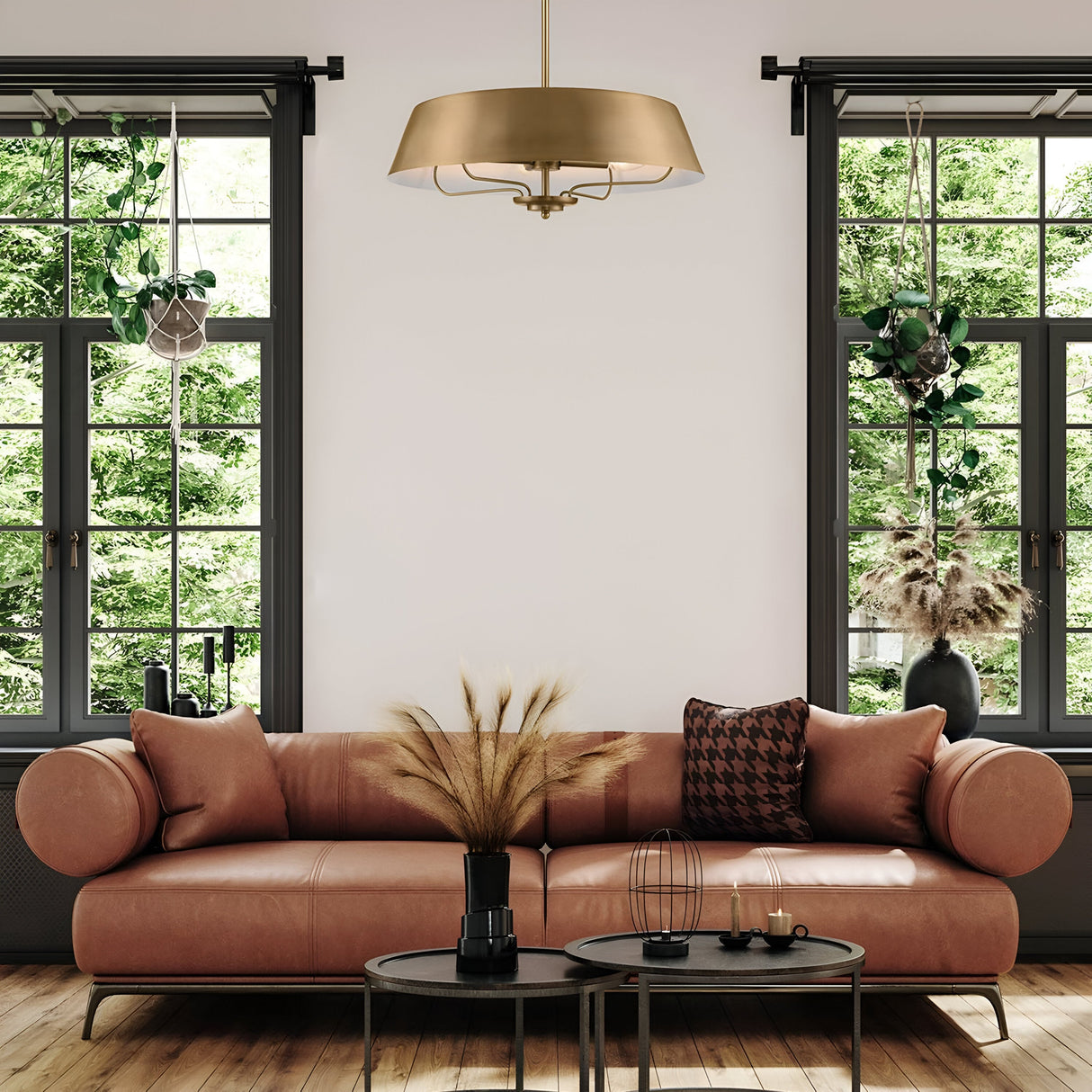 A contemporary living room featuring a peach-colored sofa adorned with decorative pillows and a coffee table decorated with dried plants. Large windows with black frames let in plenty of natural light, while hanging plants enhance the room's vibrancy. Overhead, the Luella 4 Light Duo-Mount Chandelier/Semi-Flush in brushed natural brass elegantly illuminates the space, offering versatile installation options and a view of the lush greenery outside.