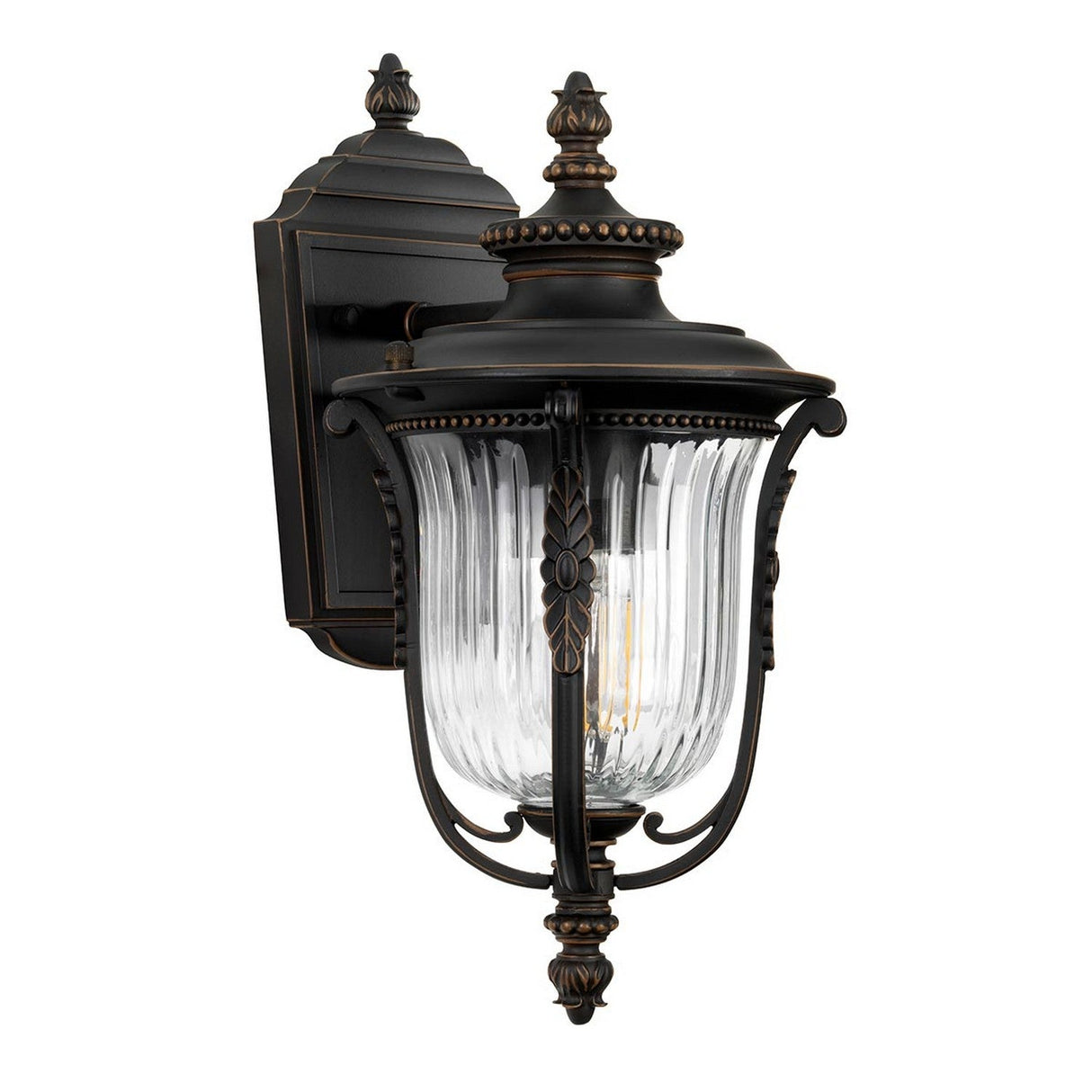 The Luverne Outdoor 1 Light Small Wall Lantern in rubbed bronze features exquisite ornamental details and a ribbed glass shade. This traditional design showcases a fluted glass encasement that gracefully accommodates a single bulb.