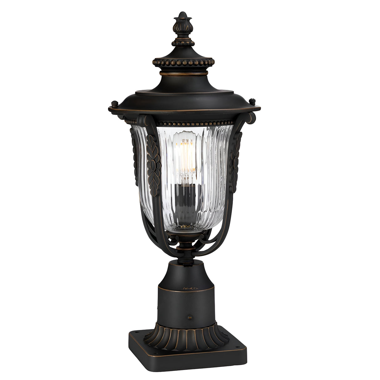The Luverne Outdoor 1 Light Medium Pedestal in rubbed bronze features a vintage-style lantern design with ornate detailing and a clear glass casing that reveals a visible bulb inside. It stands on a decorative square base with intricate carvings, evoking a classic and elegant look, and is IP44 rated for durability.