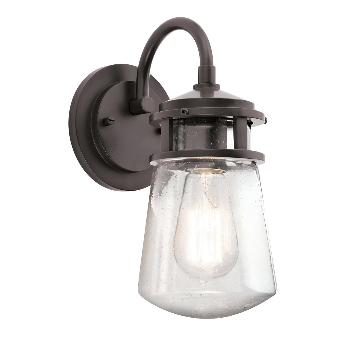 The Lyndon Outdoor 1 Light Small Wall Lantern in bronze showcases a black metal design with a clear seedy glass shade that encases an Edison-style bulb. Its curved arm and circular wall mount deliver a vintage industrial look reminiscent of an outdoor wall lantern.
