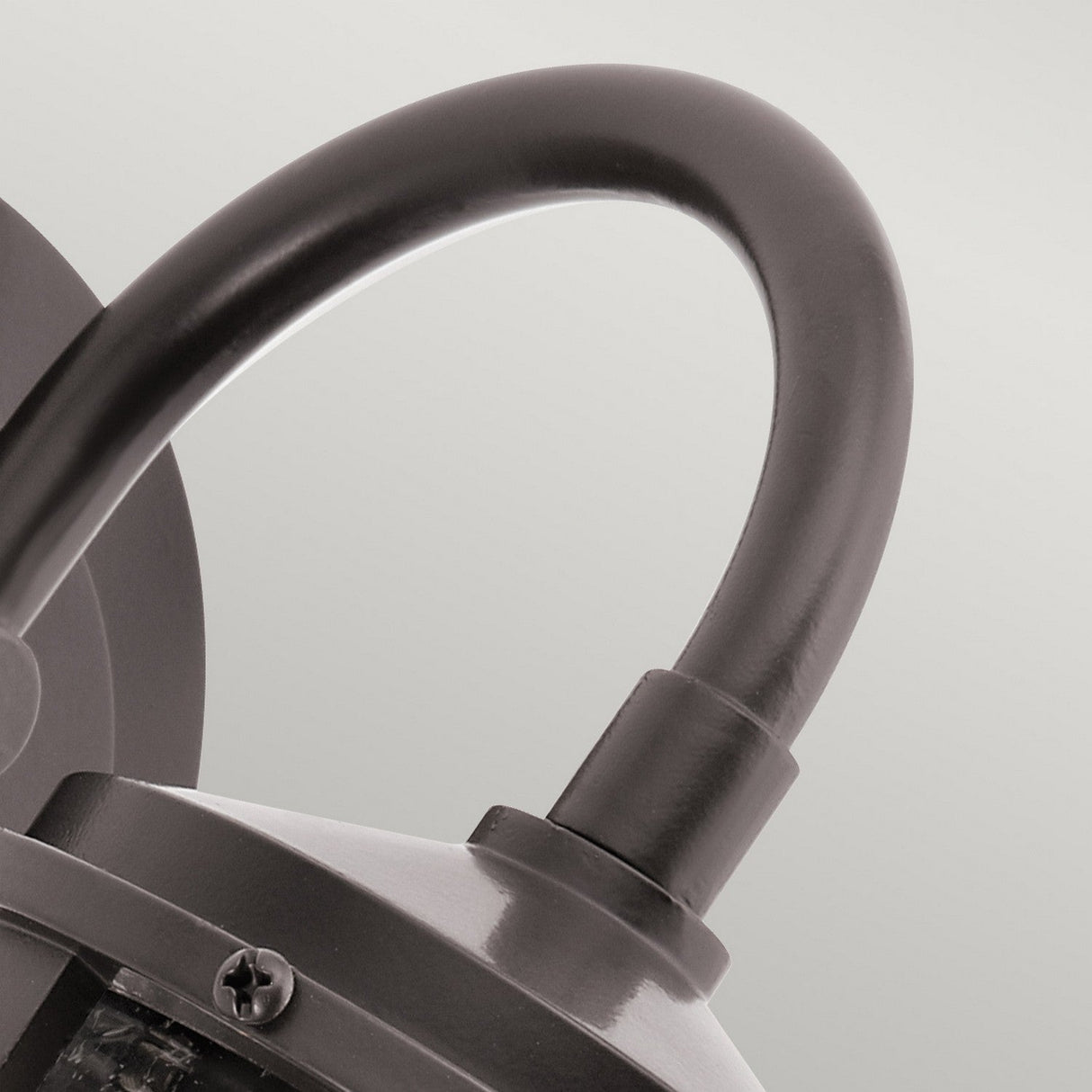 Close-up of the Lyndon Outdoor 1 Light Small Wall Lantern in bronze, showcasing its sleek design with a curved arm and semi-circular shade. The modern aesthetic, featuring smooth lines and clear seedy glass, adds elegance against a neutral background.