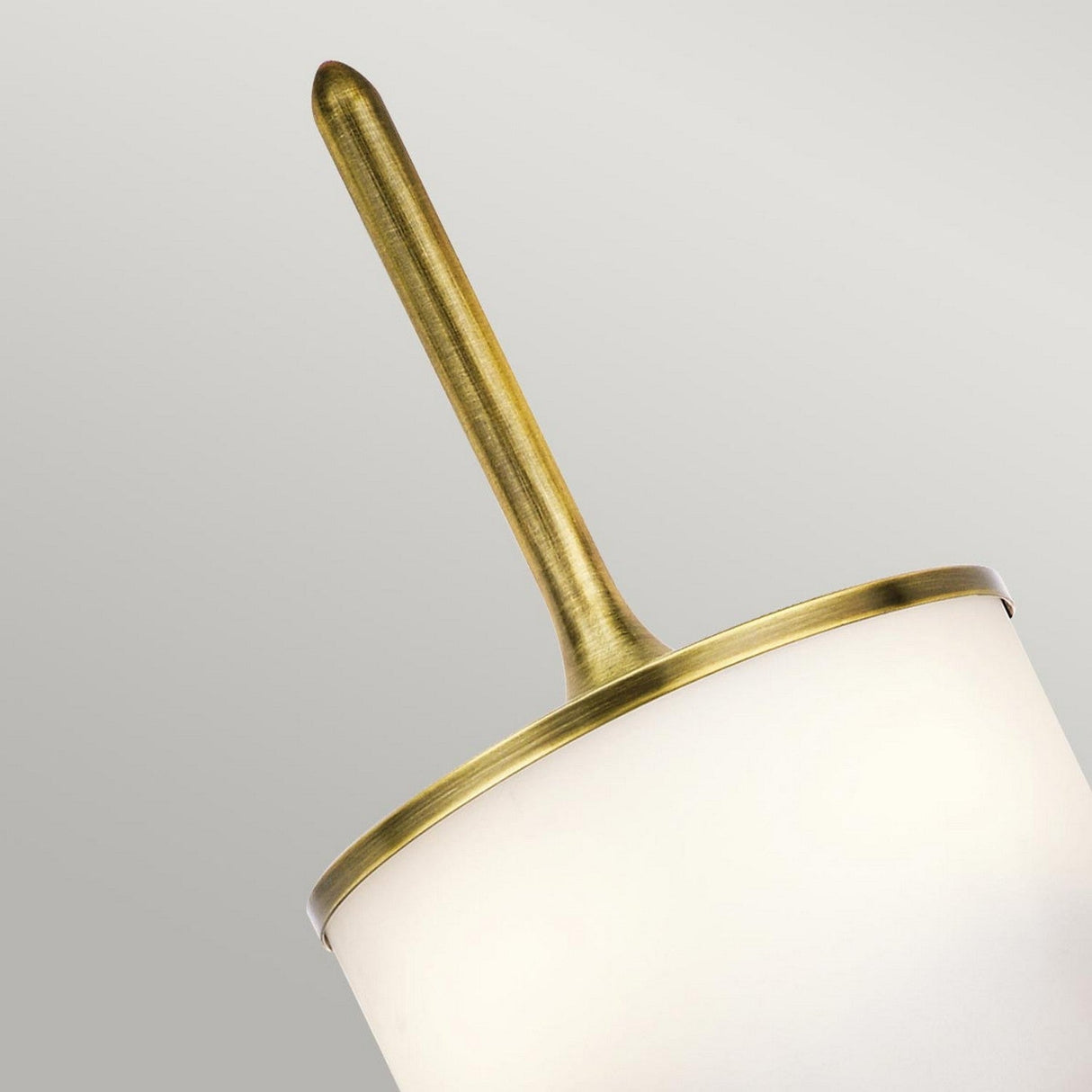 A close-up of the Mona 2 Light Small Wall Light - Natural Brass highlights its modern design infused with mid-century charm. This piece features a central natural brass rod adorned with a circular, opaque white shade that strikingly contrasts against its light background.