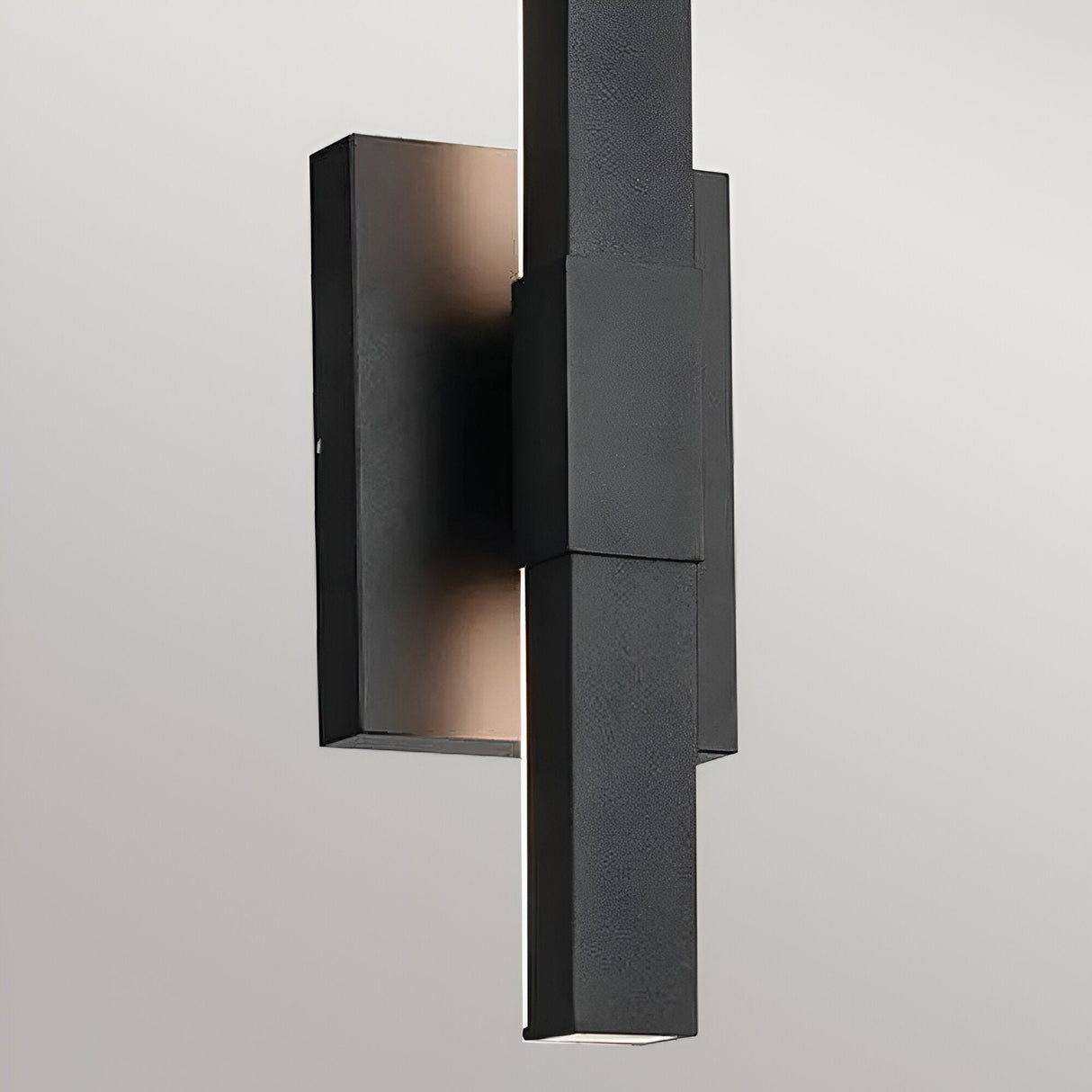 The Nocar LED Outdoor Medium Wall Light 20W 3000K in black features clean, geometric lines on a rectangular backplate and emits a subtle glow from behind the central vertical bar when mounted on a light gray wall.