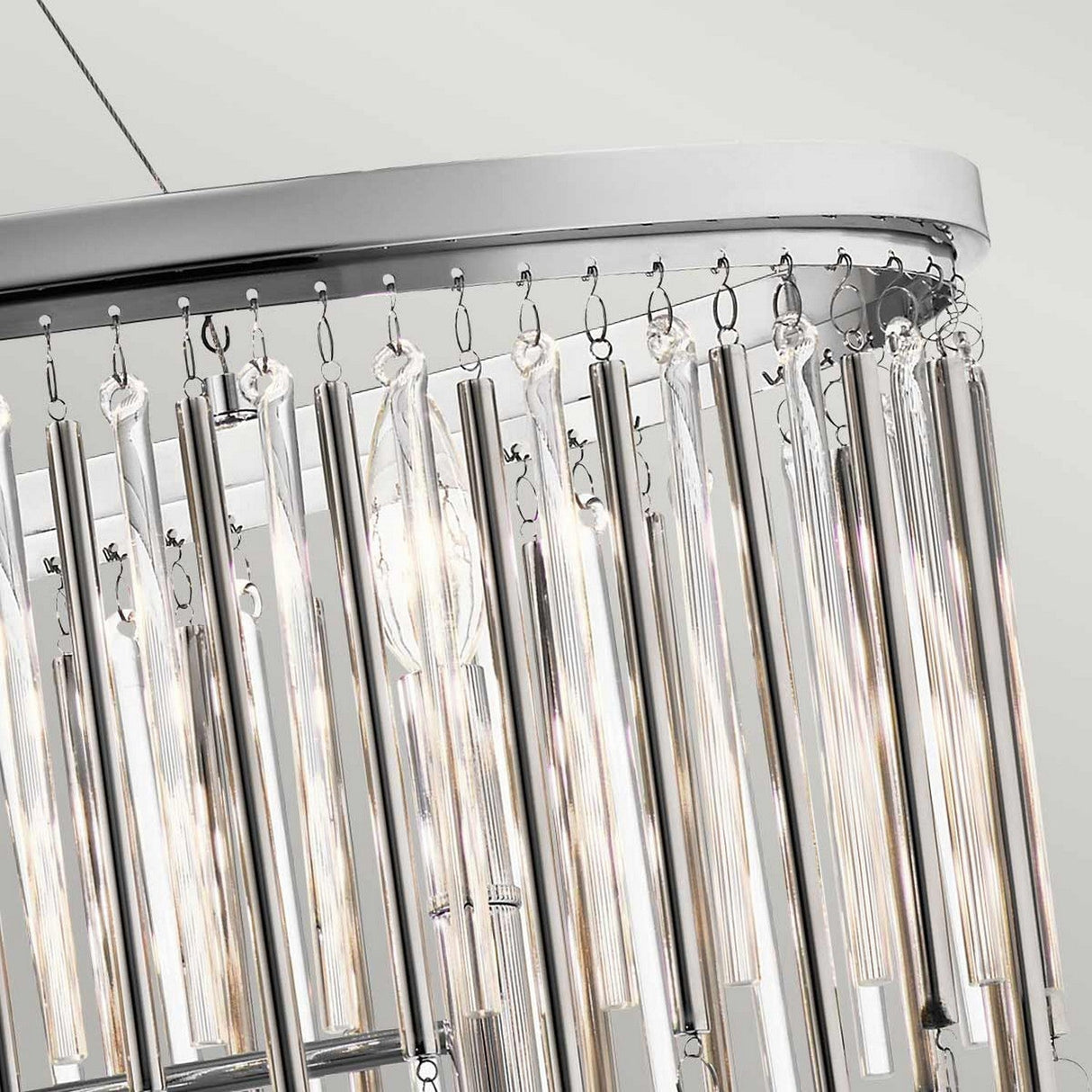 Close-up of the Piper 6 Light Oval Chandelier in polished chrome, featuring cylindrical metal and clear glass rods arranged in a row. Glass bead accents beautifully reflect light to create a shimmering effect against the soft, neutral background.