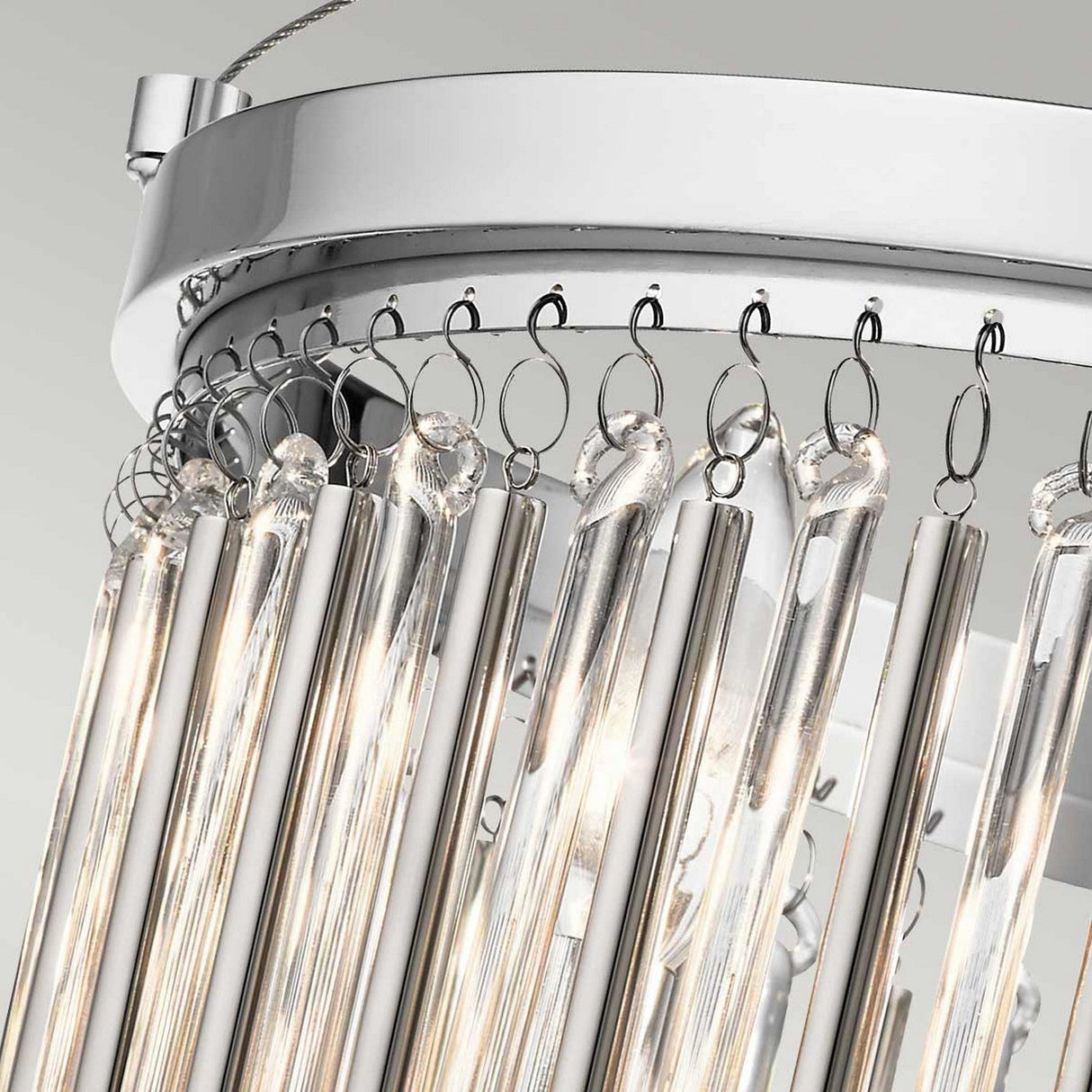 Close-up of a contemporary chandelier showcasing vertical glass rods hanging from a circular metallic frame finished in polished chrome. The illuminated rods, accompanied by delicate glass bead accents, create a radiant and sophisticated look against a light gray background similar to the Piper 3 Light Semi Flush - Polished Chrome.